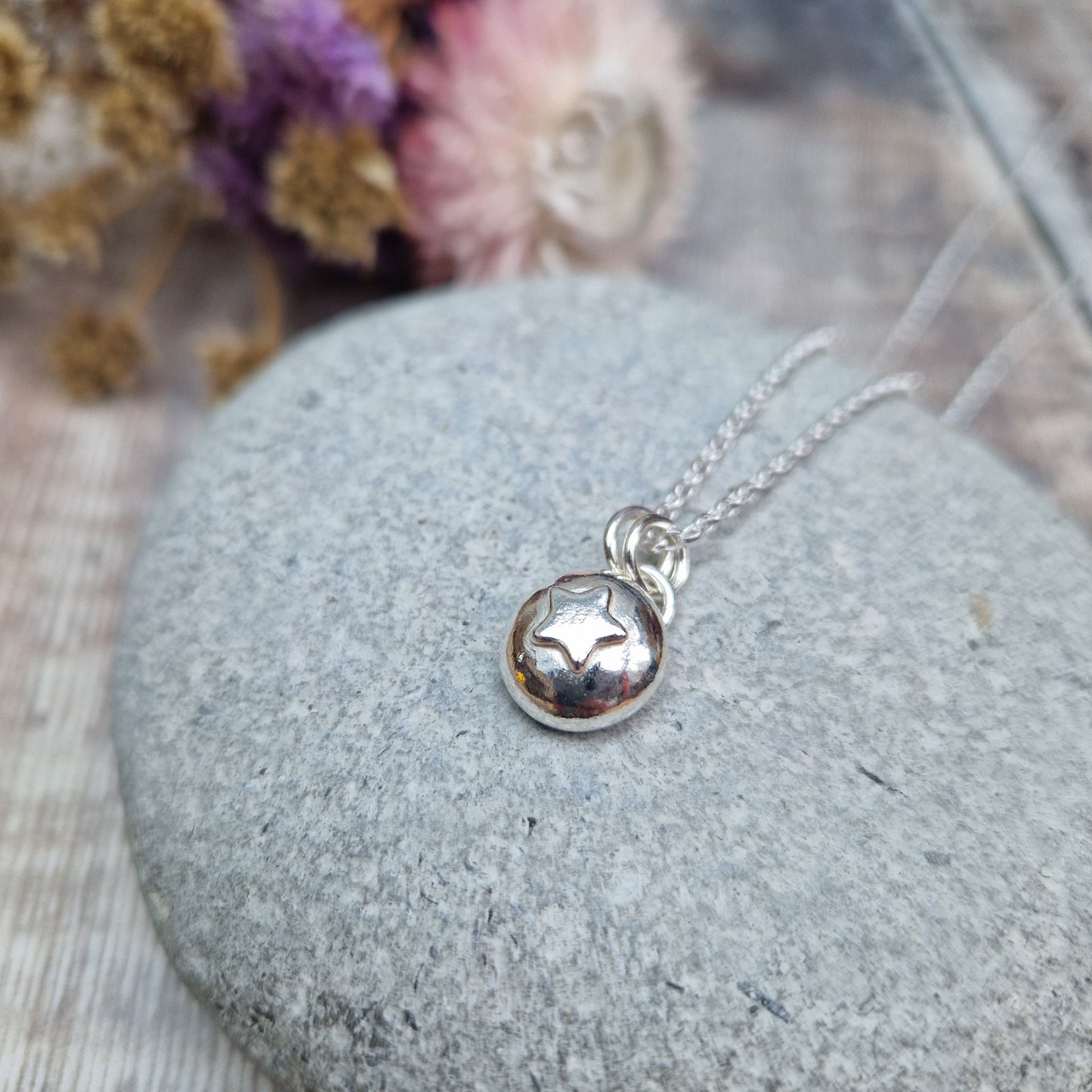 Sterling Silver round pebble shaped pendant with slightly raised silver five-pointed star shape at its centre. Suspended from a silver via two small silver circle links.