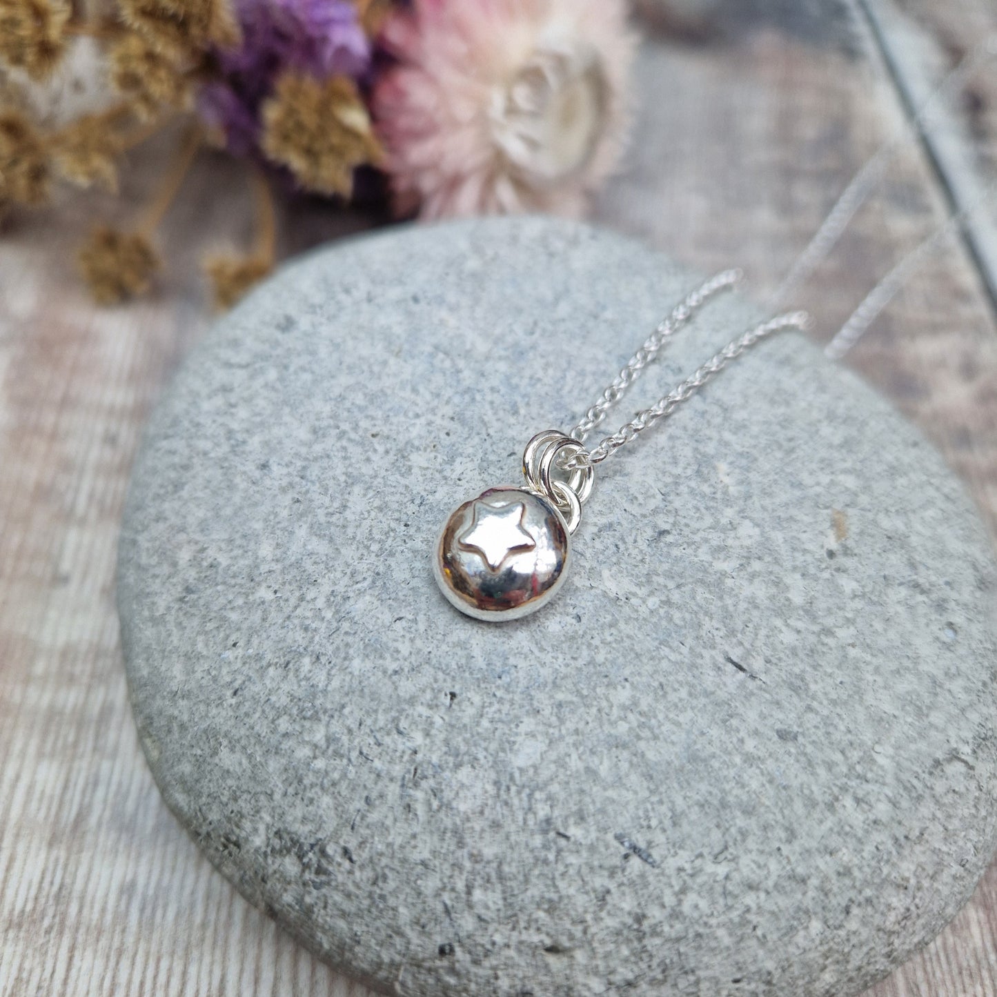 Sterling Silver round pebble shaped pendant with slightly raised silver five-pointed star shape at its centre. Suspended from a silver via two small silver circle links.