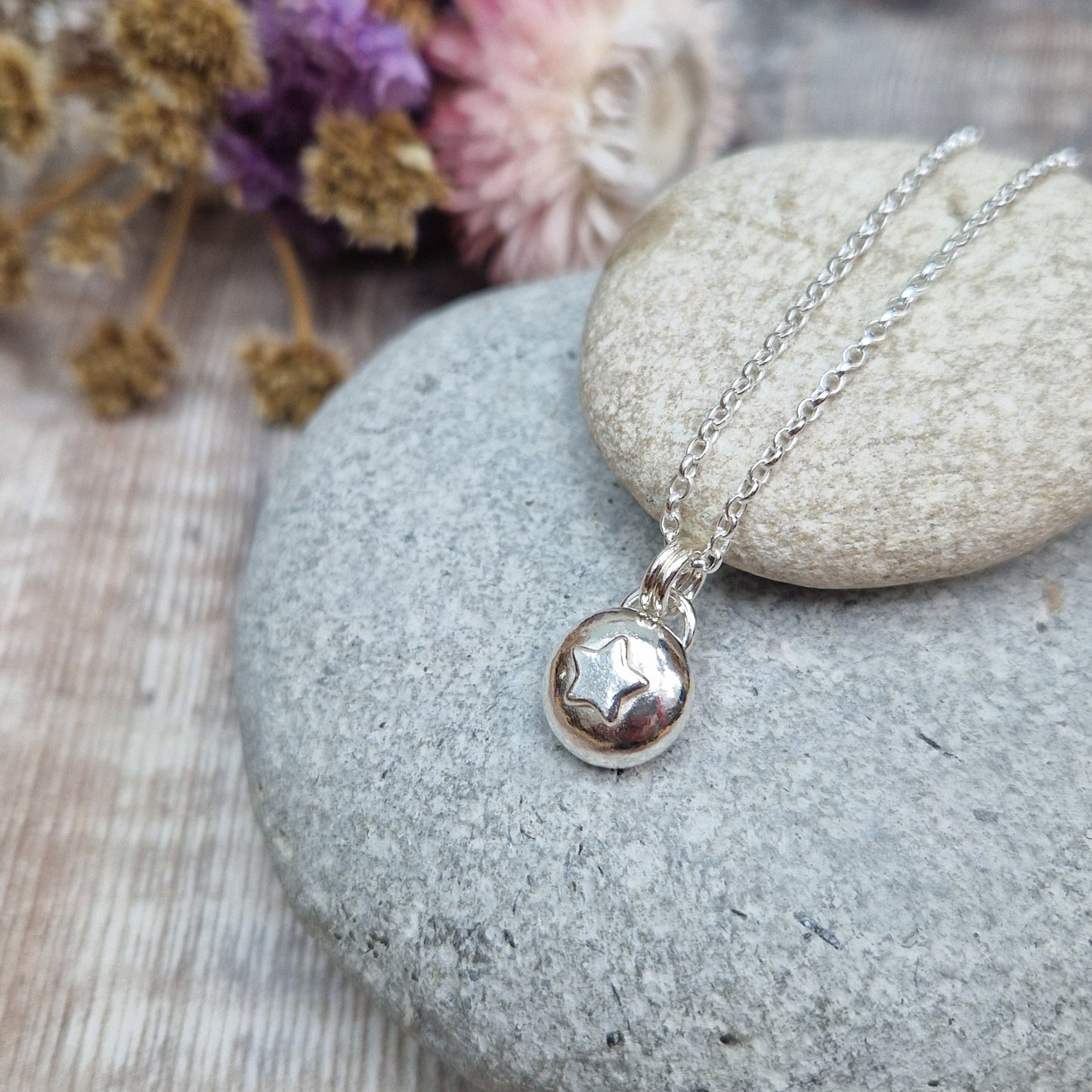 Sterling Silver round pebble shaped pendant with slightly raised silver five-pointed star shape at its centre. Suspended from a silver via two small silver circle links.