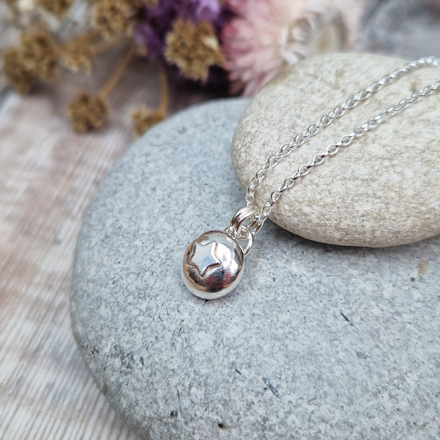 Sterling Silver round pebble shaped pendant with slightly raised silver five-pointed star shape at its centre. Suspended from a silver via two small silver circle links.