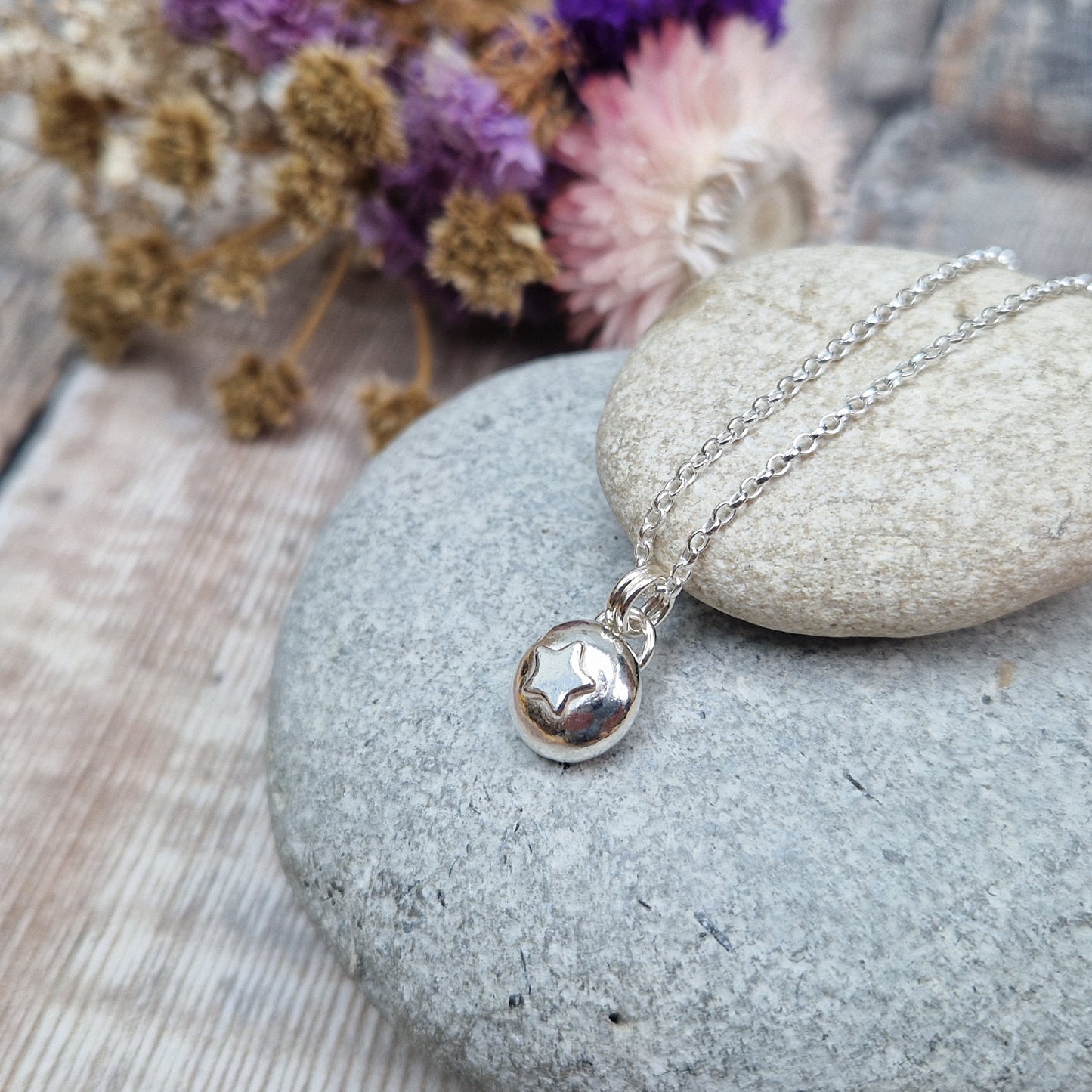 Sterling Silver round pebble shaped pendant with slightly raised silver five-pointed star shape at its centre. Suspended from a silver via two small silver circle links.