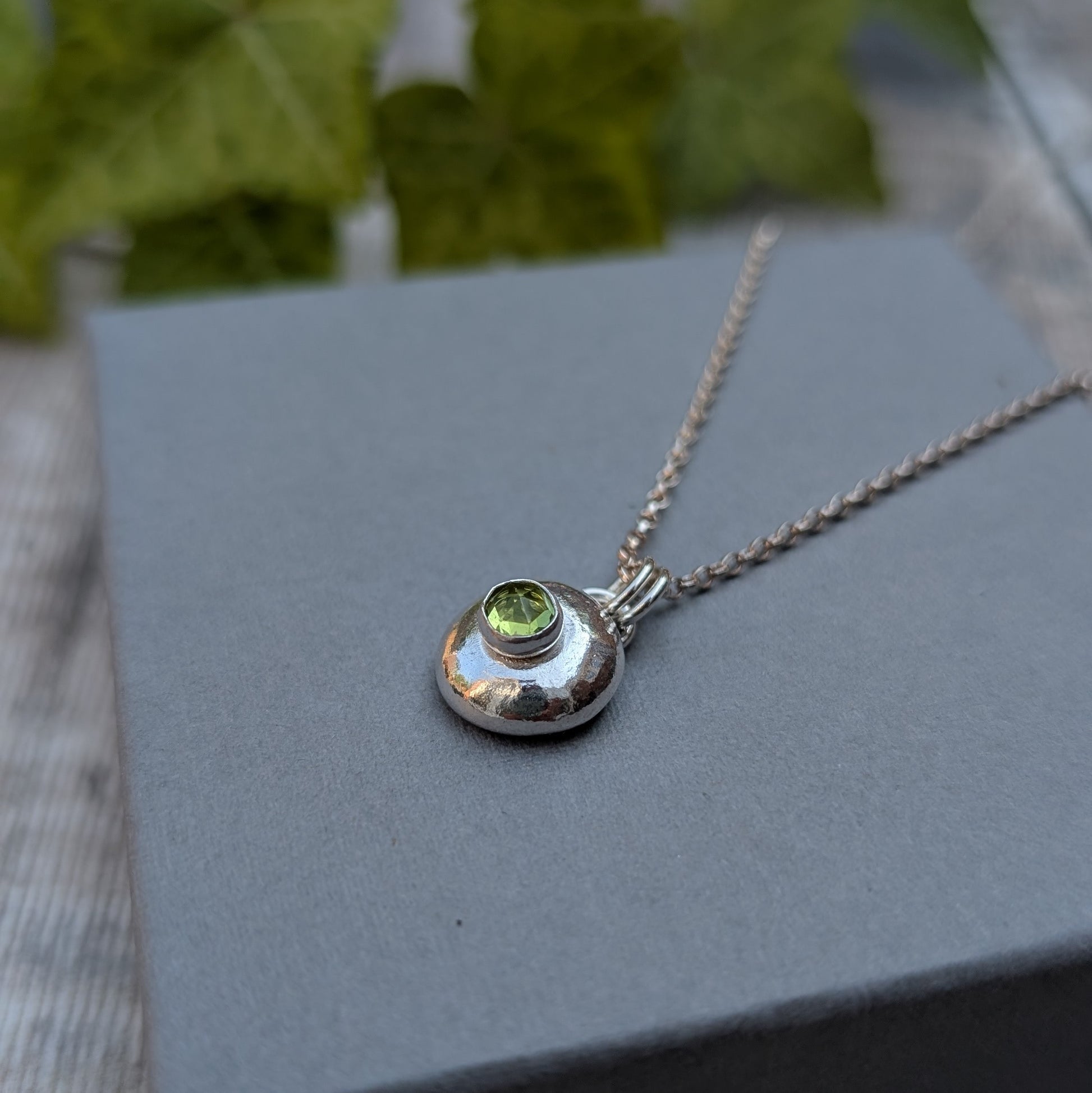 Peridot pebble necklace handmade from recycled Sterling Silver with a polished silver pebble pendant and faceted green Peridot gemstone on a silver chain.