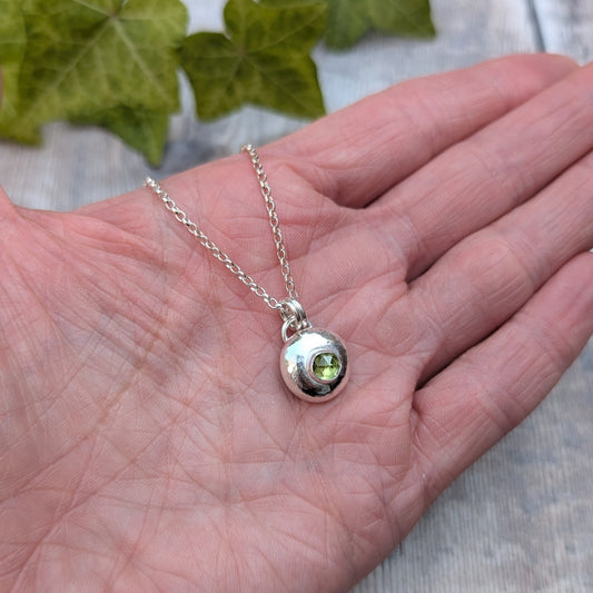 Peridot pebble necklace resting in the palm of a hand, showing the size of the handmade recycled Sterling Silver pebble pendant with a faceted Peridot gemstone.