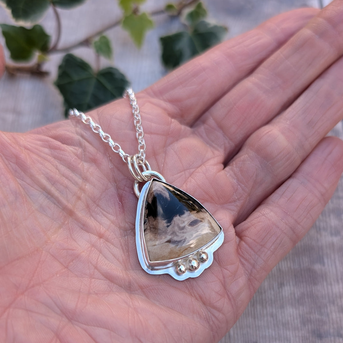 Petrified Palm Wood Statement Gemstone Necklace resting in the palm of a hand, showing the natural patterns of the triangular gemstone, polished silver setting and three decorative silver balls.
