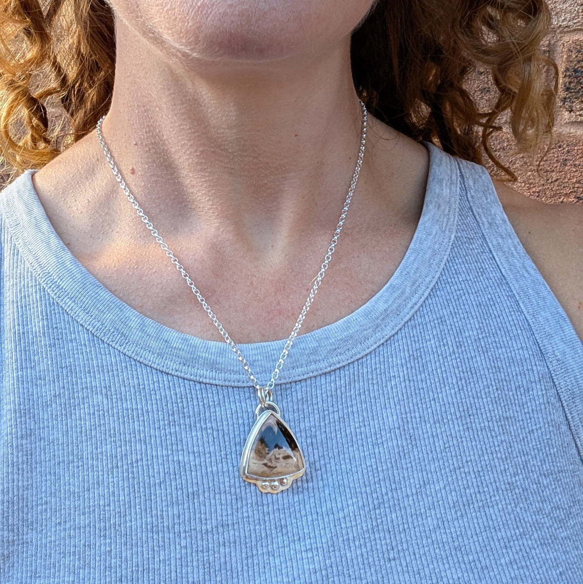 Petrified Palm Wood Statement Gemstone Necklace being worn on a sterling silver chain, showing the size and length of the triangular gemstone pendant against a light blue top.