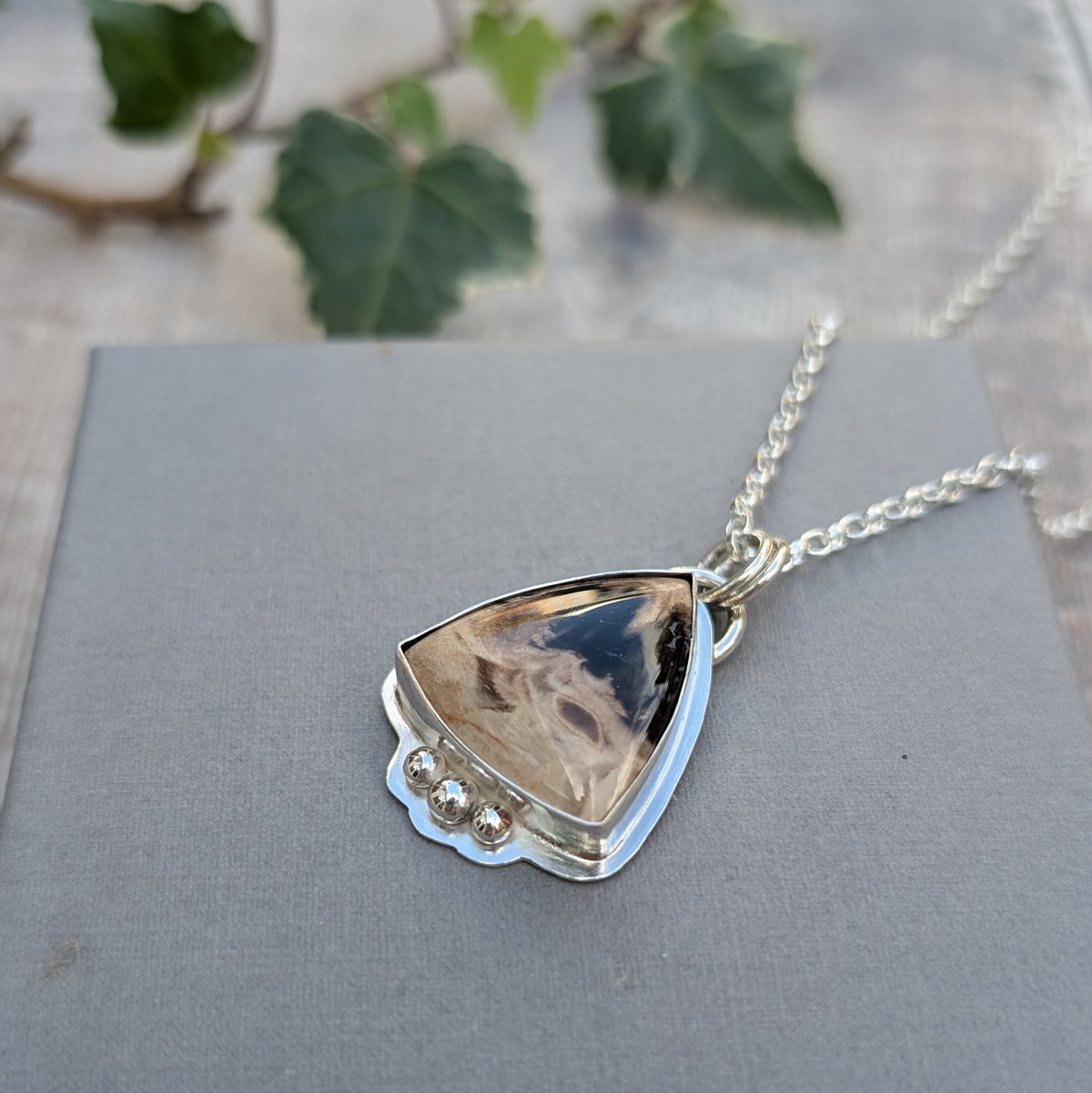 Petrified Palm Wood Statement Gemstone Necklace resting on a grey background, showing the natural black, brown and cream markings of the gemstone and handmade silver setting.