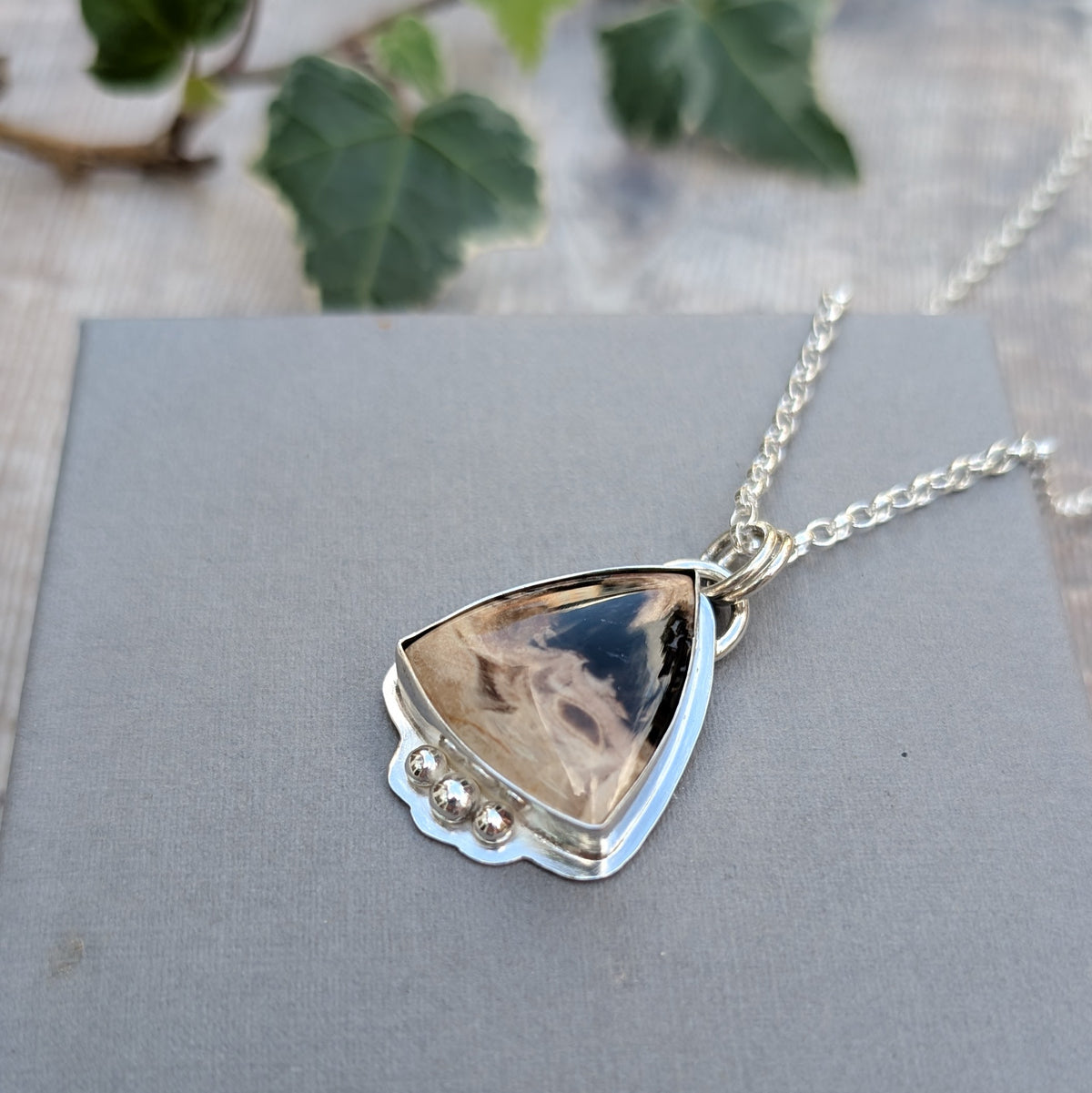 Petrified Palm Wood Statement Gemstone Necklace photographed at an angle on a grey background with green ivy, showing the polished gemstone and silver ball details.