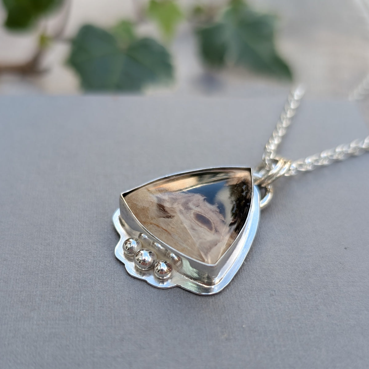 Close up of the Petrified Palm Wood Statement Gemstone Necklace, showing the triangular stone with natural dark and cream patterns, handmade silver bezel and three silver balls.