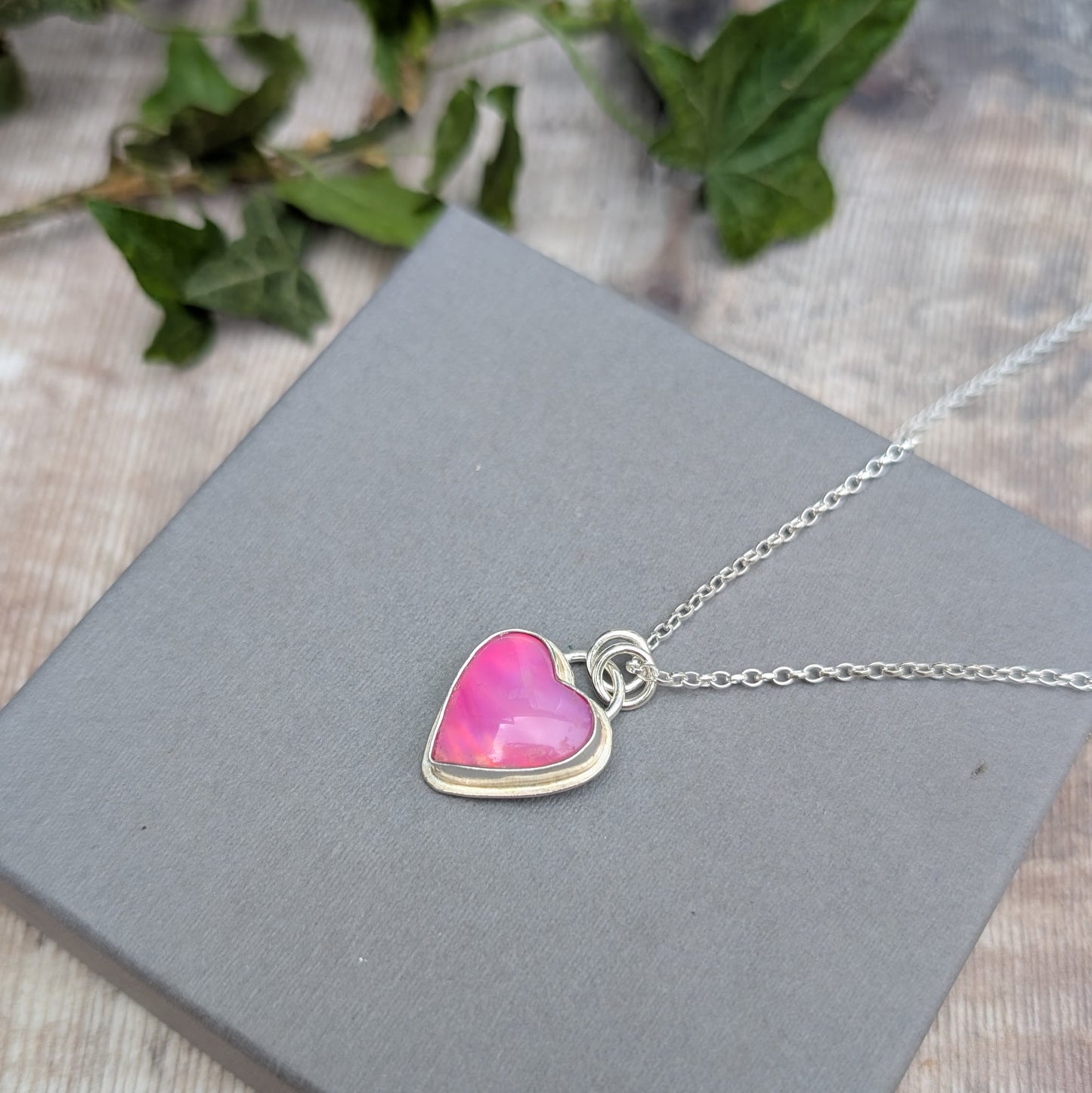 Pink Aurora Opal Heart Necklace handmade from recycled Sterling Silver, shown on a grey jewellery box with ivy leaves in the background.