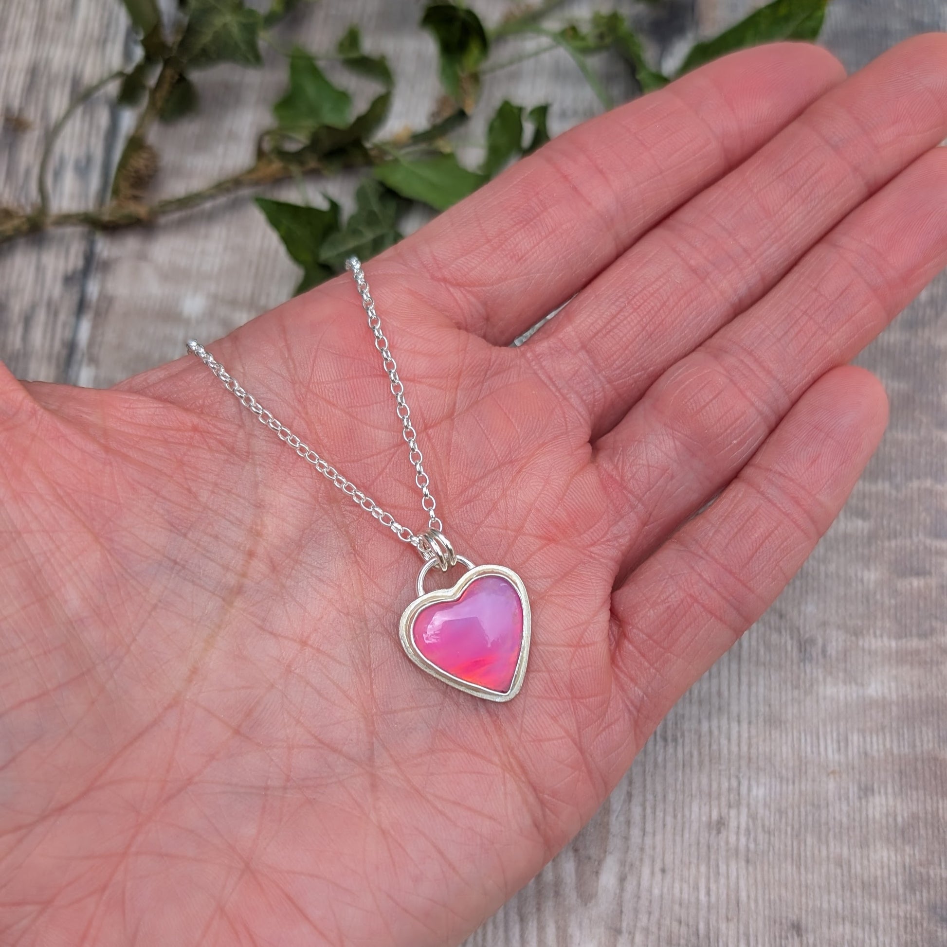 Pink Aurora Opal Heart Necklace handmade from recycled Sterling Silver shown resting in the palm of a hand to demonstrate size.