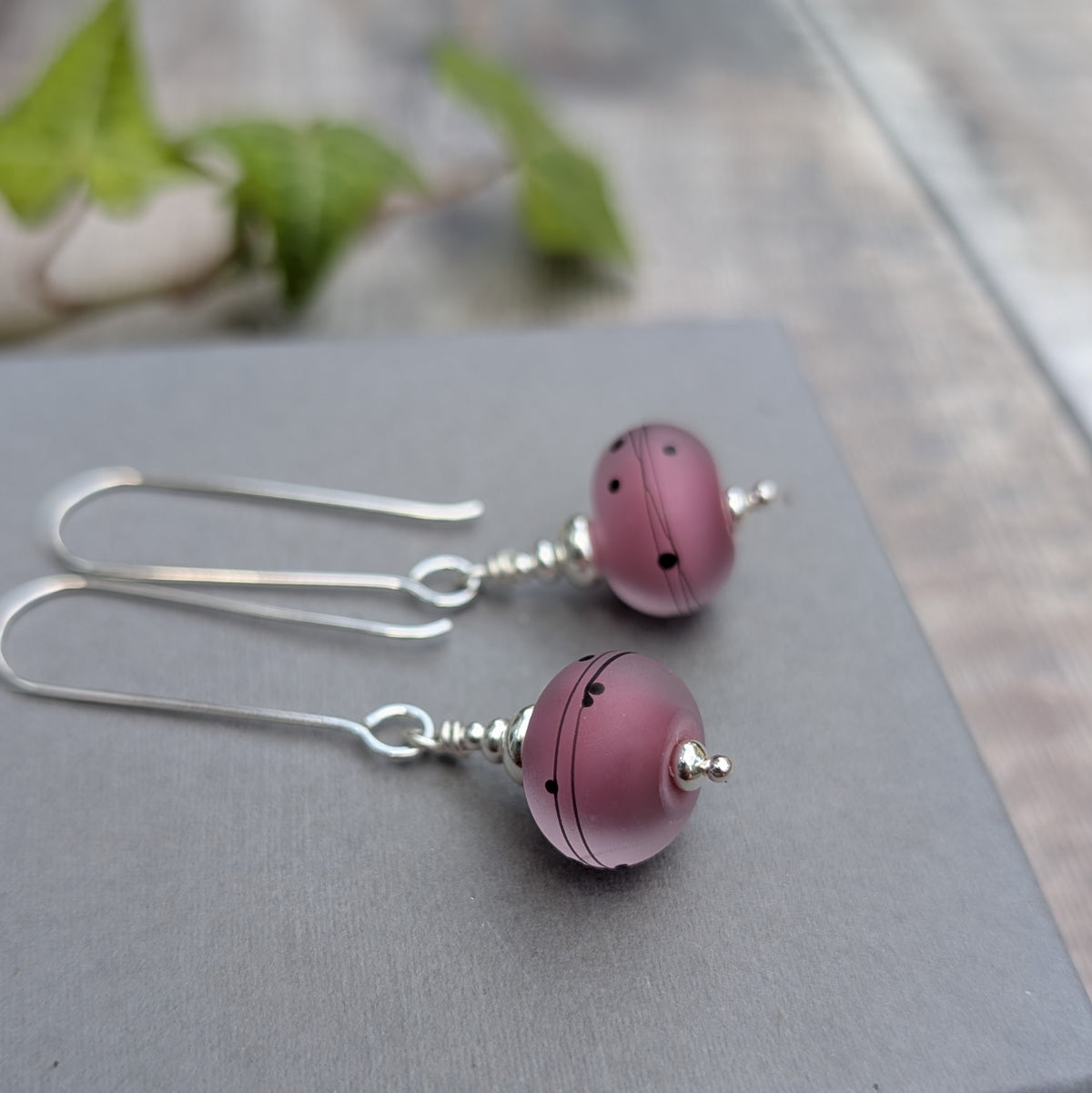 Close up of pink scribbles lampwork glass long silver earrings on a grey background, showing the handmade pink Lampwork beads and silver details.