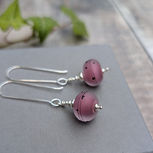 Close up of pink scribbles lampwork glass long silver earrings on a grey background, showing the handmade pink Lampwork beads and silver details.