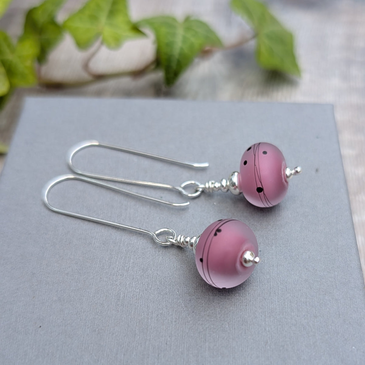 Close up of pink scribbles lampwork glass long silver earrings showing handmade frosted pink Lampwork glass beads with dark line and dot details.