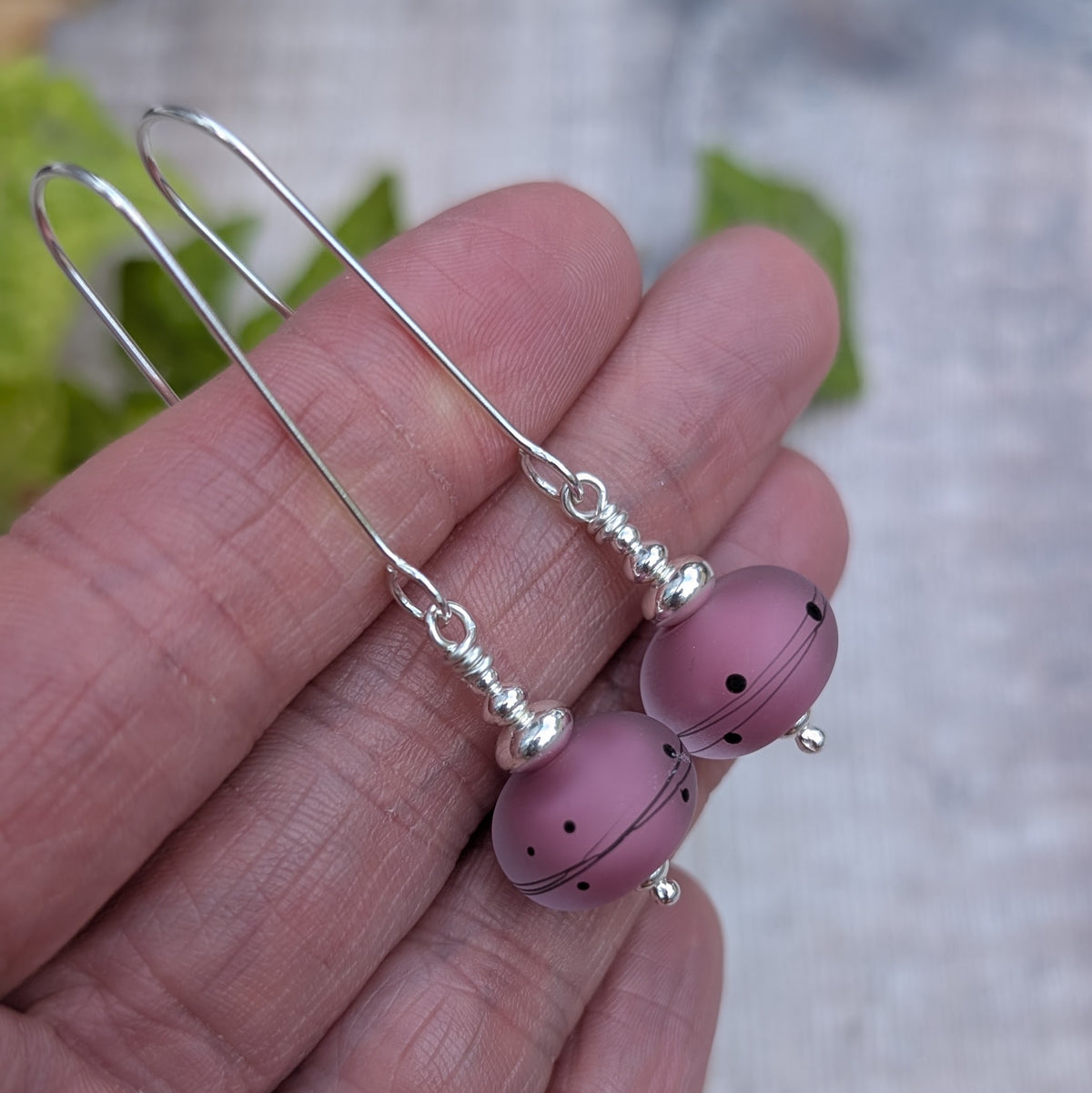 pink scribbles lampwork glass long silver earrings held in a hand, showing the handmade pink glass beads and long recycled Sterling Silver ear wires.