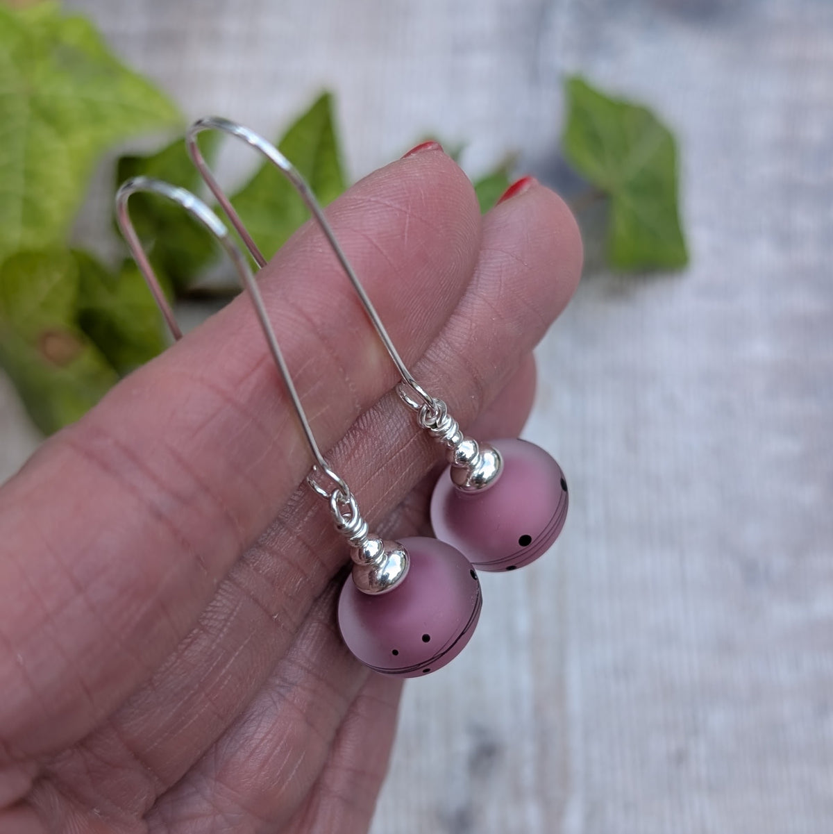 Close up of pink scribbles lampwork glass long silver earrings held in a hand, showing the frosted pink beads with black scribble and dot patterns.