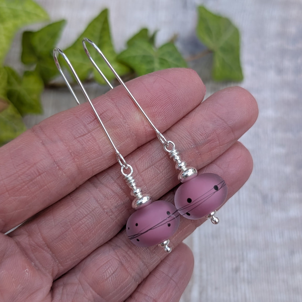 pink scribbles lampwork glass long silver earrings held in a hand to show the length of the silver ear wires and handmade Lampwork glass beads.