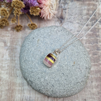 Rectangular shaped, surfite pendant set in silver bezel. The stone has horizontal stripes of gold, brown, gold, pale pink to white, almost translucent. Slightly raised stone with glossy finish. Attached to silver chain via two small circular silver links.