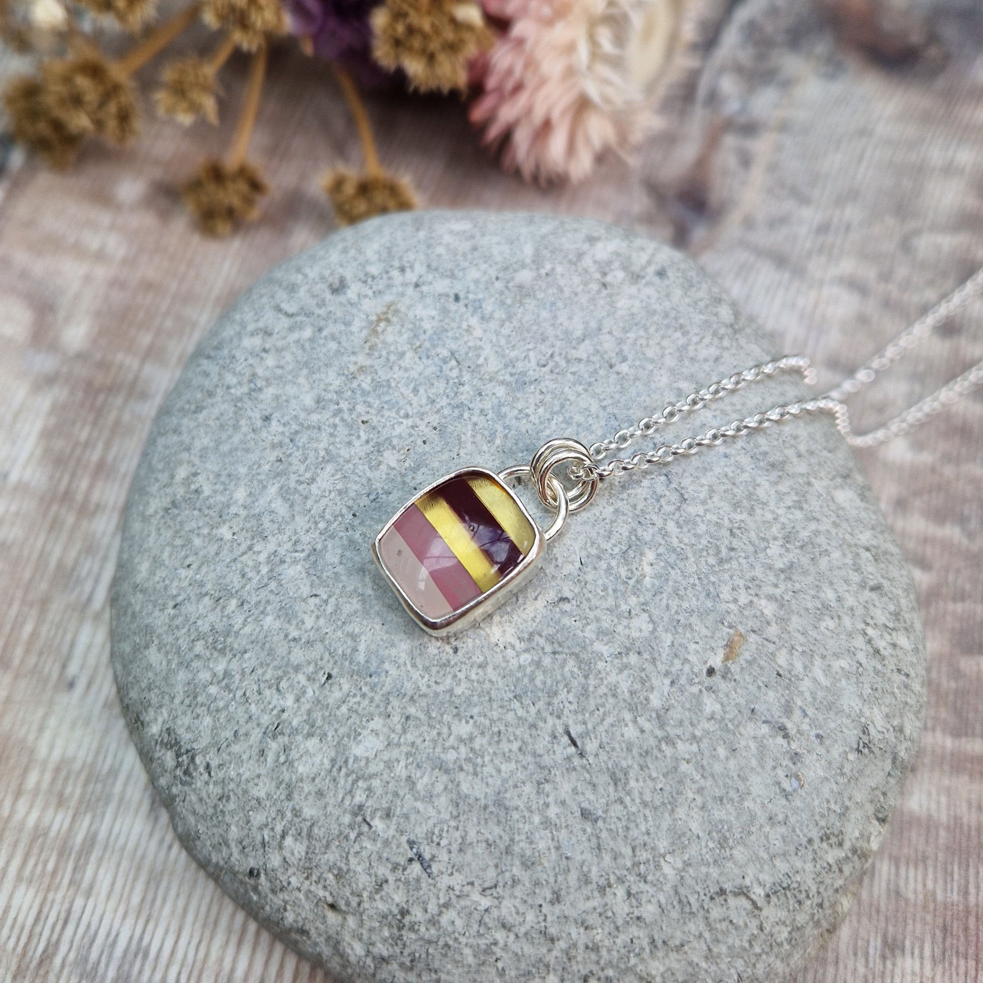 Rectangular shaped, surfite pendant set in silver bezel. The stone has horizontal stripes of gold, brown, gold, pale pink to white, almost translucent. Slightly raised stone with glossy finish. Attached to silver chain via two small circular silver links.