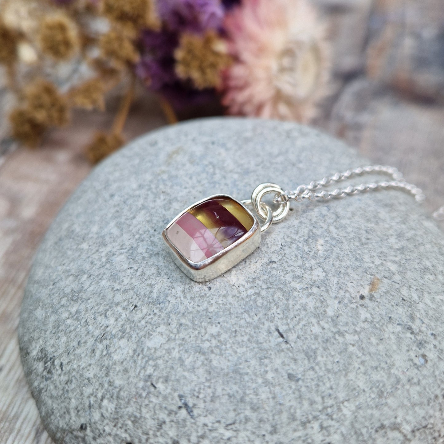 Rectangular shaped, surfite pendant set in silver bezel. The stone has horizontal stripes of gold, brown, gold, pale pink to white, almost translucent. Slightly raised stone with glossy finish. Attached to silver chain via two small circular silver links.