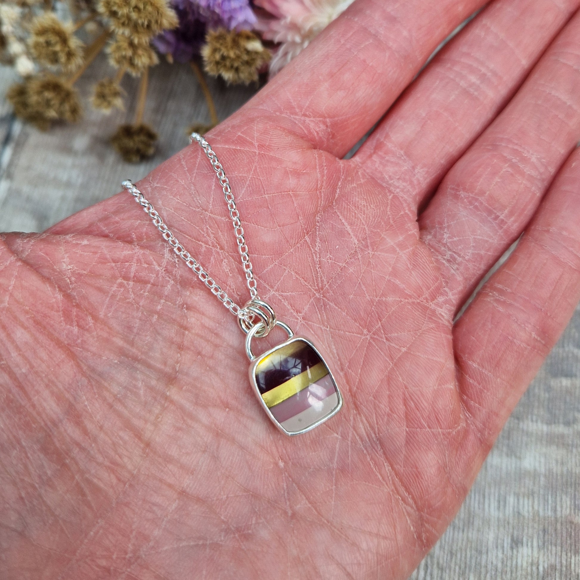 Rectangular shaped, surfite pendant set in silver bezel. The stone has horizontal stripes of gold, brown, gold, pale pink to white, almost translucent. Slightly raised stone with glossy finish. Attached to silver chain via two small circular silver links.