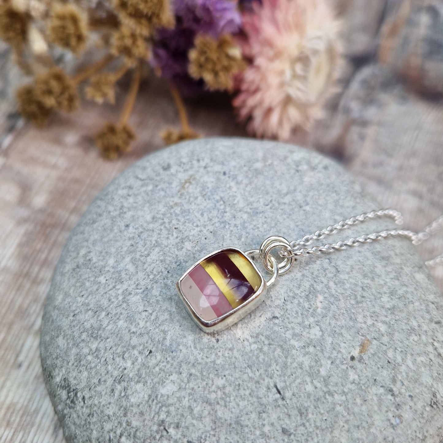 Rectangular shaped, surfite pendant set in silver bezel. The stone has horizontal stripes of gold, brown, gold, pale pink to white, almost translucent. Slightly raised stone with glossy finish. Attached to silver chain via two small circular silver links.