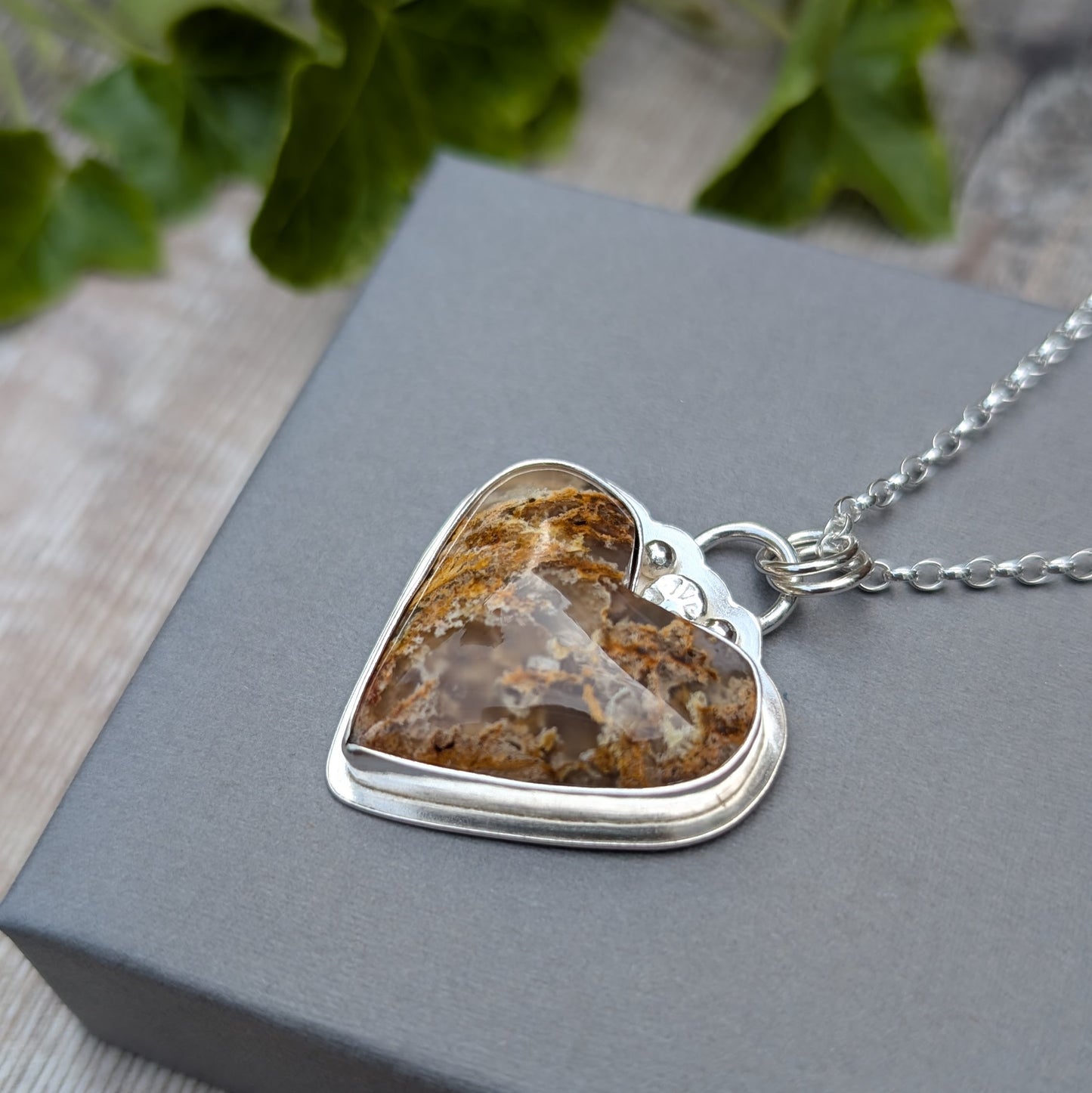 Close-up angled view of Plume Agate Heart Necklace on box showing natural plume patterns in the stone