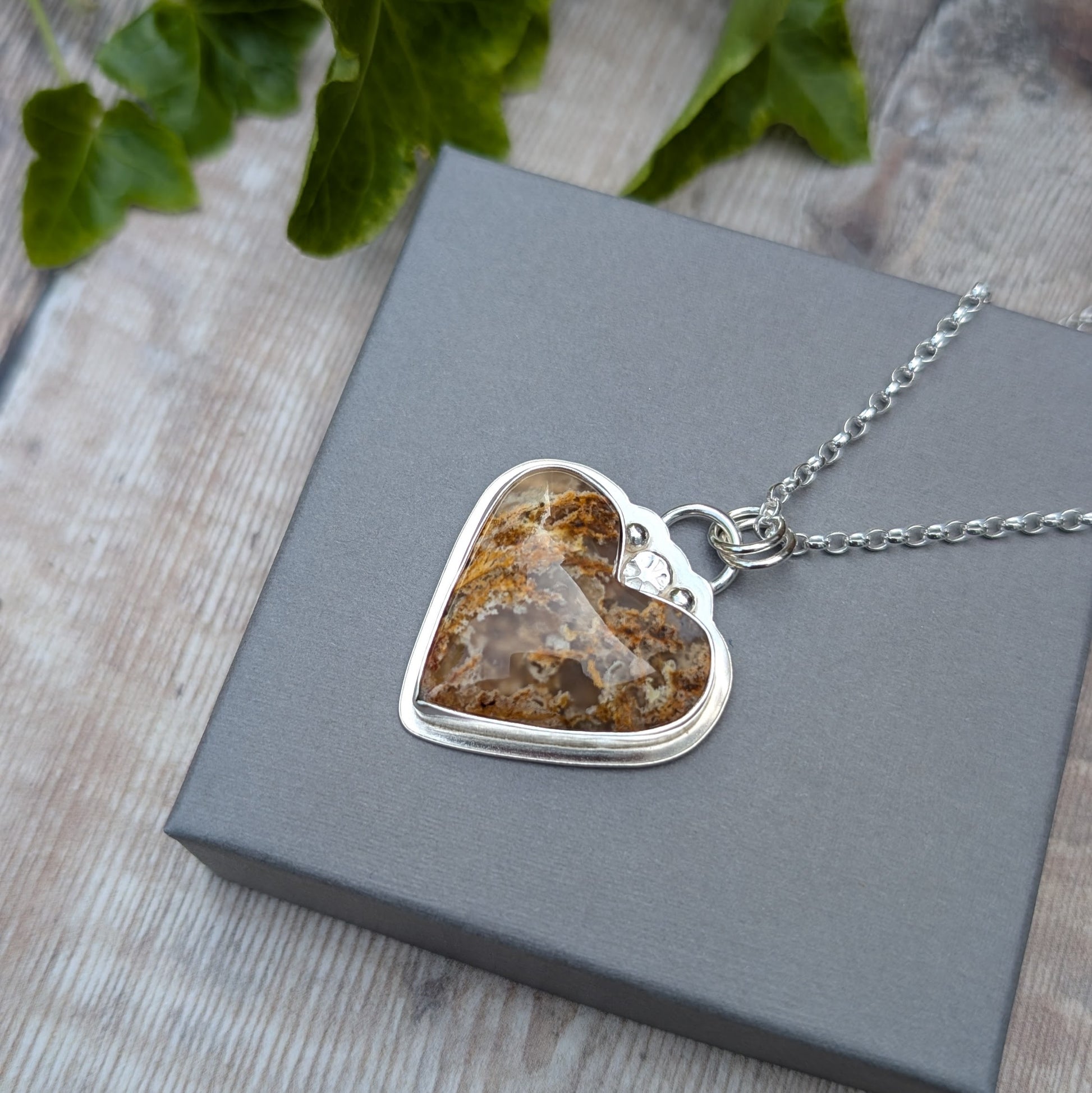 Plume Agate Heart Necklace on a grey box showing front of heart-shaped stone set in recycled sterling silver