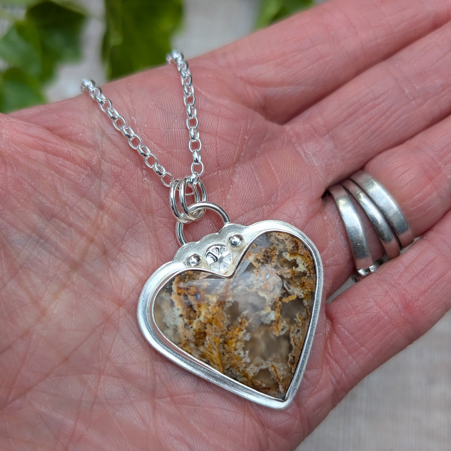 Close-up of Plume Agate Heart Necklace held in hand showing natural stone patterns and silver detail