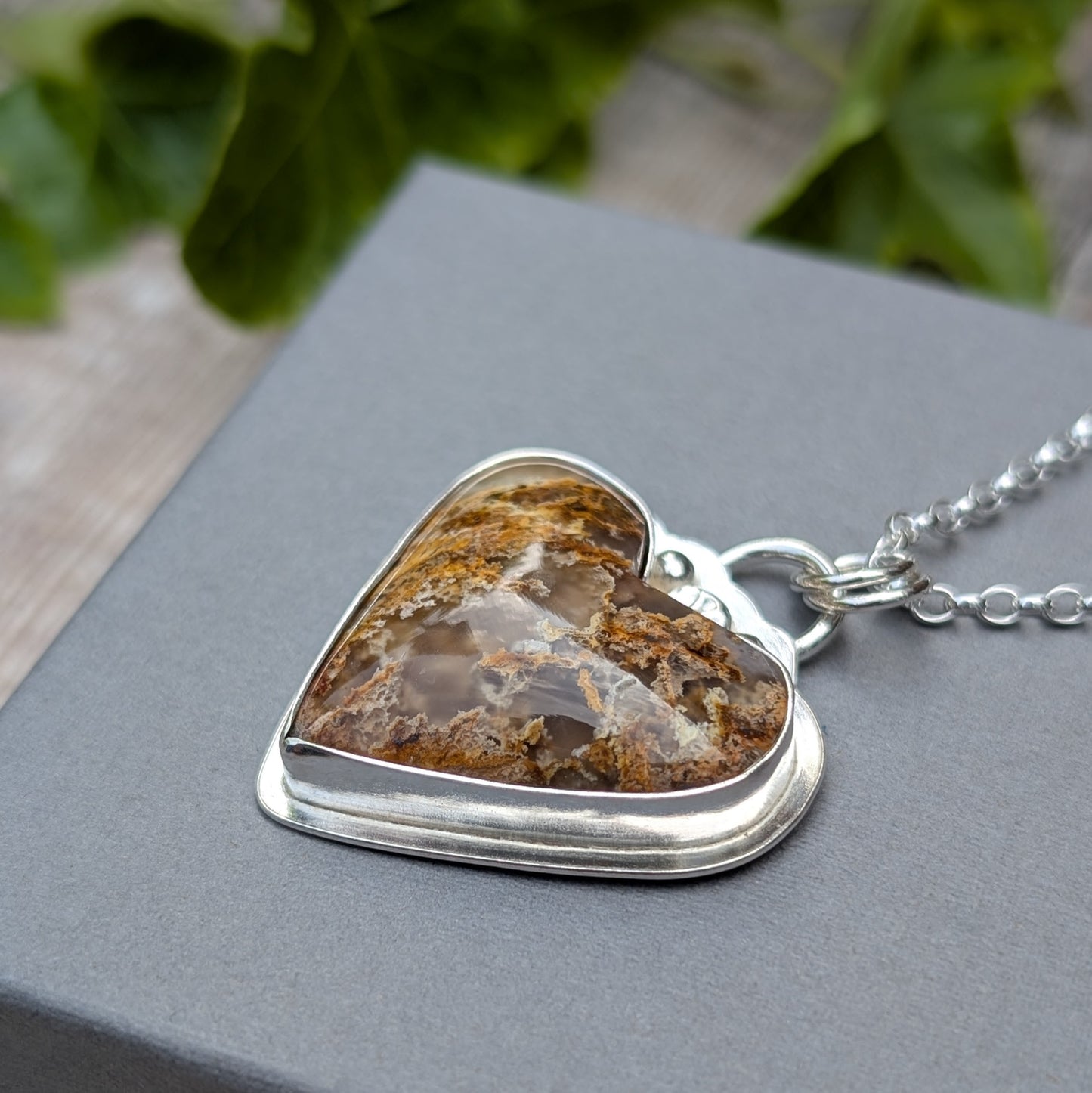 Side angle of Plume Agate Heart Necklace highlighting depth of stone and handmade silver setting