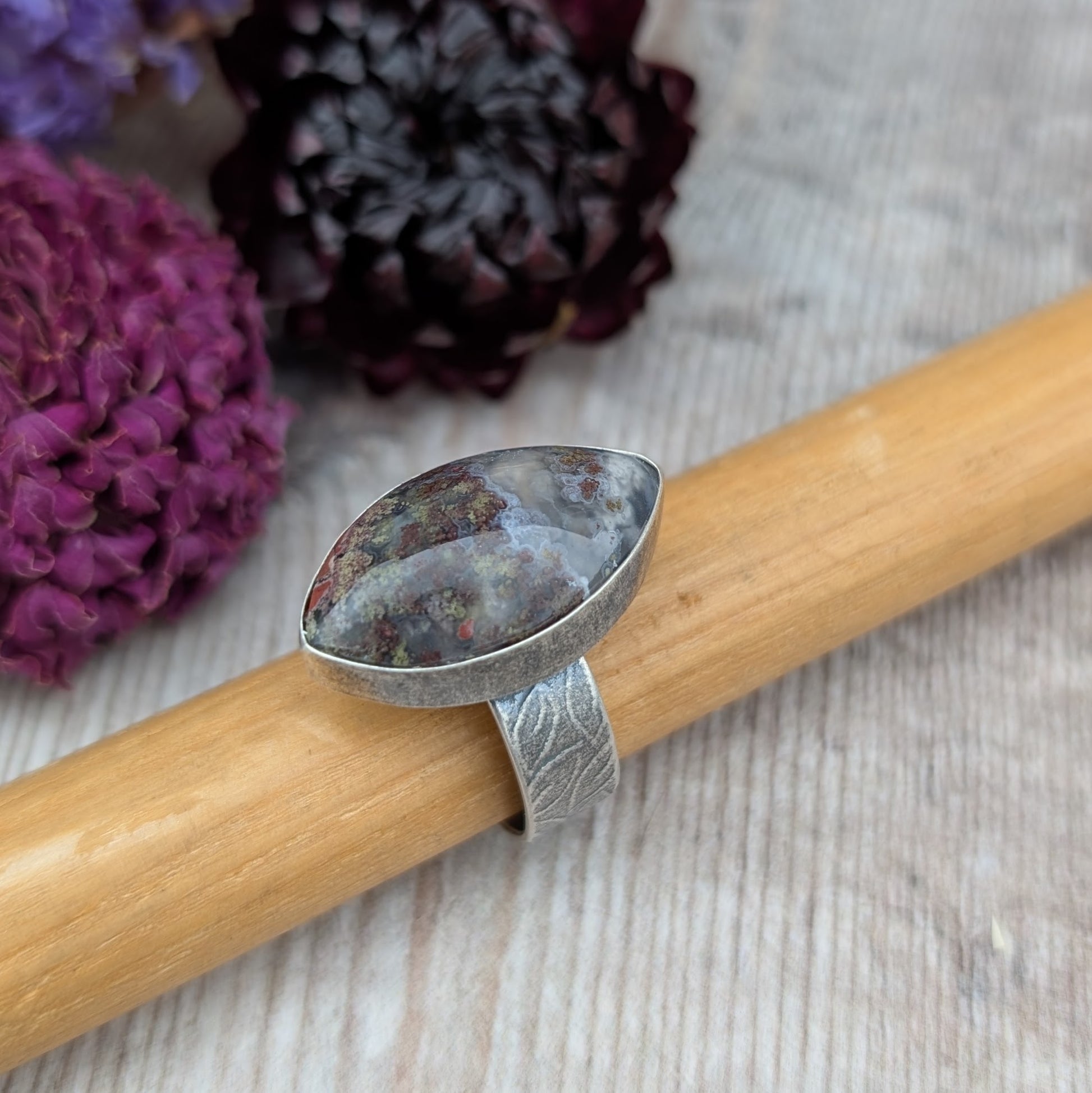 Silver Plume Agate Ring resting on a wooden ring holder, showing marquise shaped stone with natural plume patterns and handmade silver setting