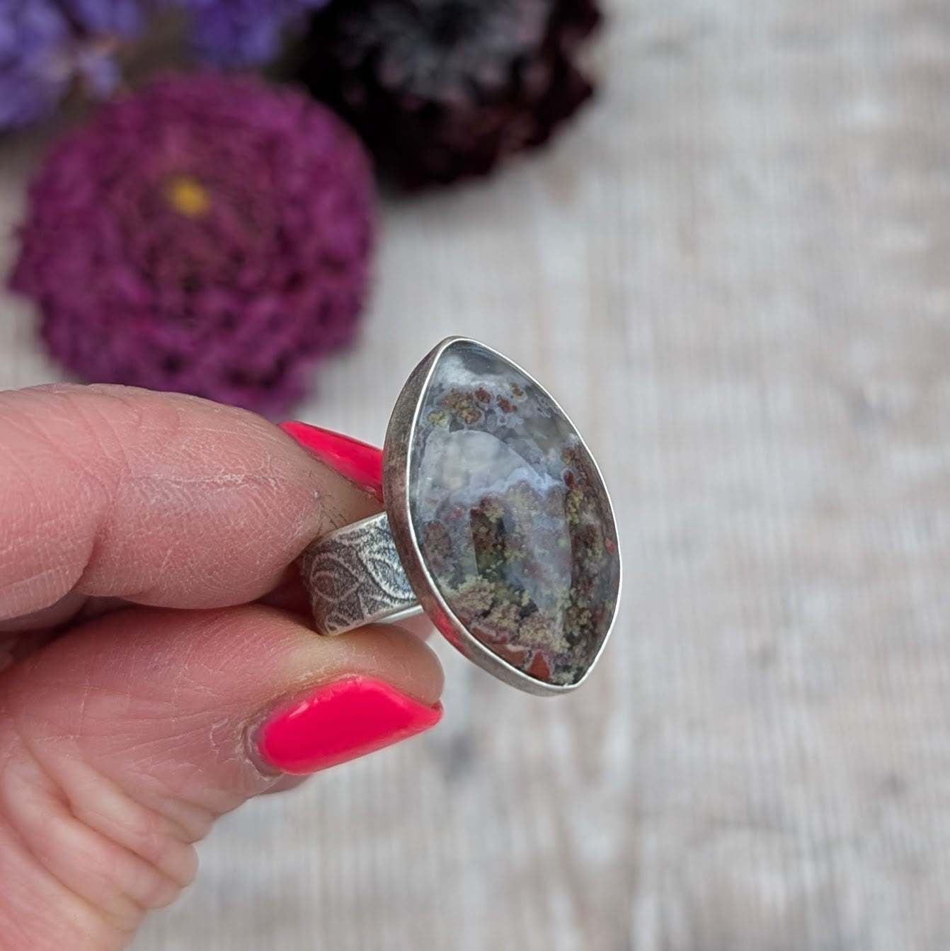 Silver Plume Agate Ring held between fingers, showing marquise plume agate stone with grey, brown and green natural patterns
