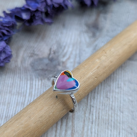 Heart-shaped Surfite ring displayed on a wooden ring mandrel, highlighting the colourful layers and hammered silver band.