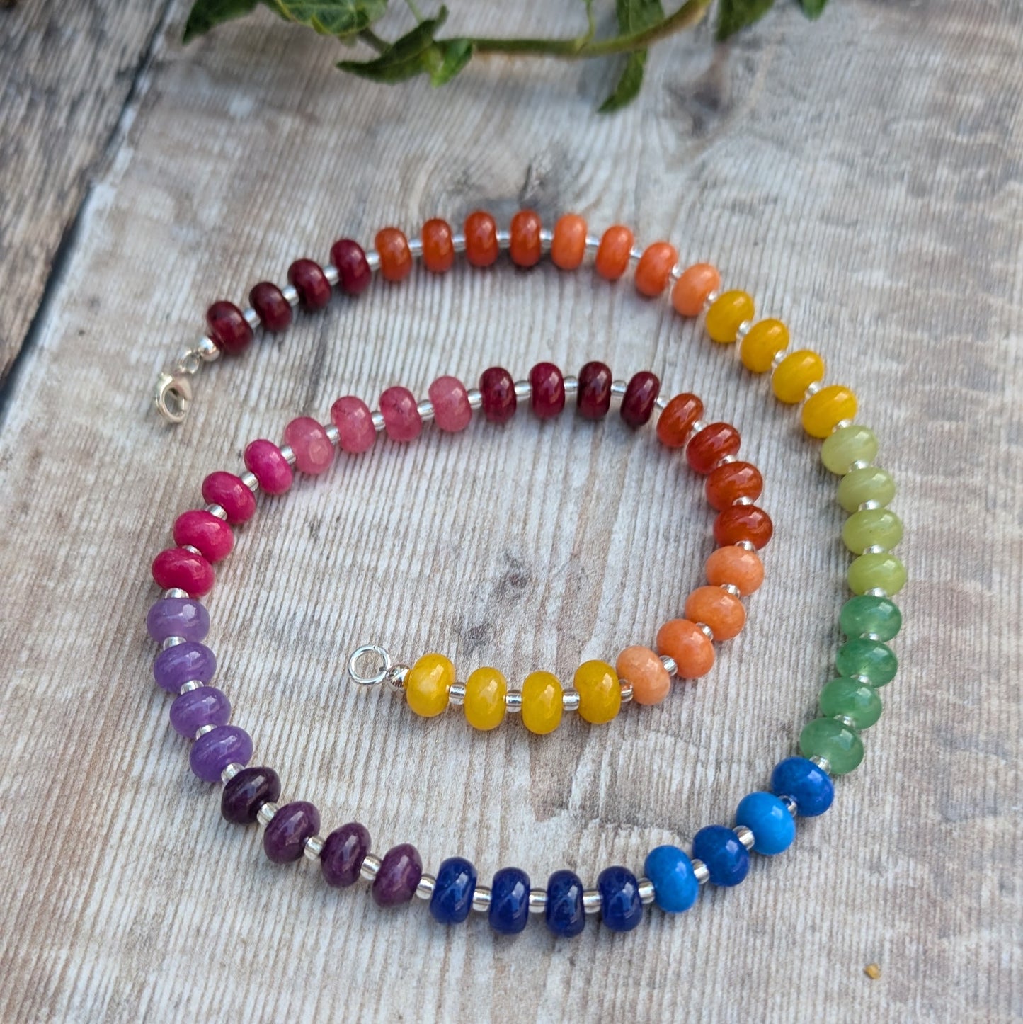 Rainbow Jade Bead Necklace laid out on a wooden surface, showing the full strand of colourful jade beads and Sterling Silver clasp.