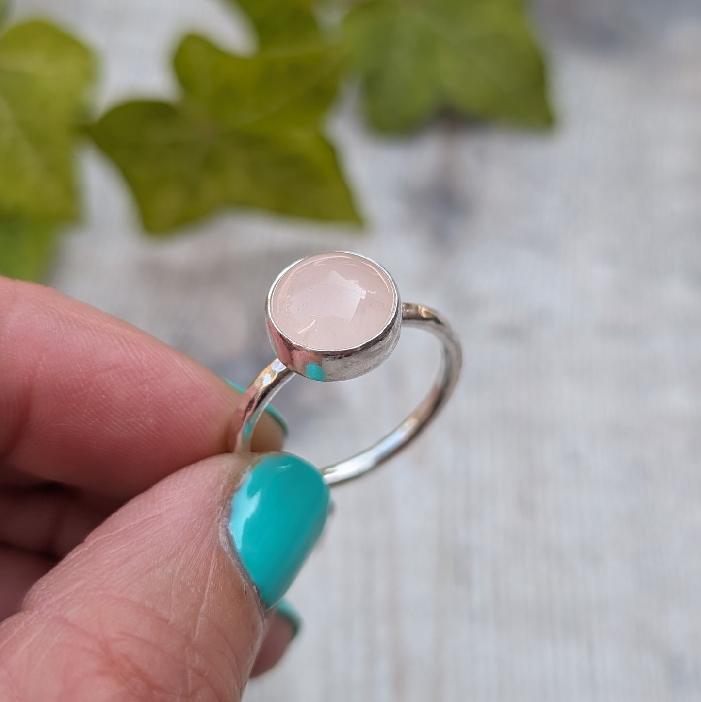 Angled close up of a rose quartz ring size R handmade from recycled Sterling Silver with a round rose quartz gemstone in a polished bezel setting.
