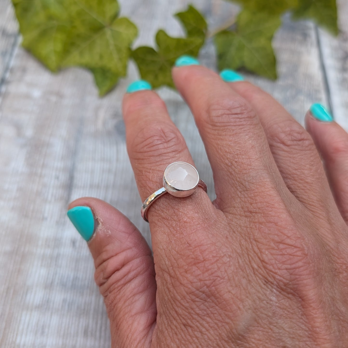 Rose quartz ring size R worn on a finger, handmade from recycled Sterling Silver with a polished round rose quartz gemstone in a bezel setting.