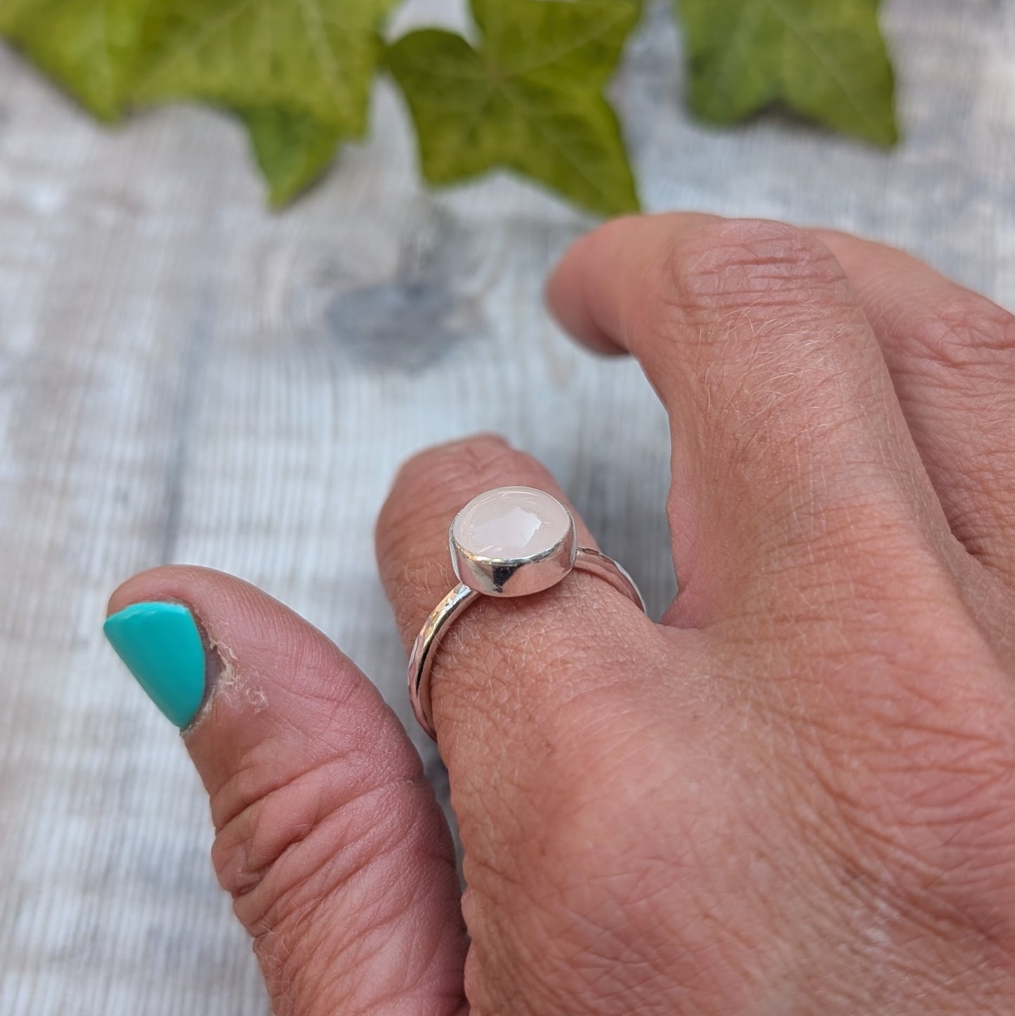 Side view of a rose quartz ring size R on a hand, showing the recycled Sterling Silver band and raised bezel set rose quartz gemstone.