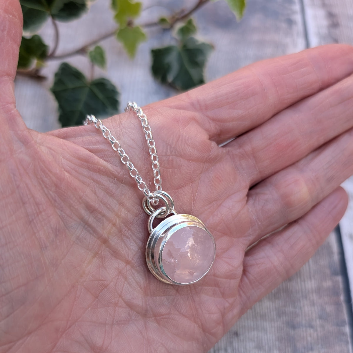 Rose Quartz Statement Gemstone Necklace handmade from recycled sterling silver, featuring a round pale pink gemstone in a polished silver setting, resting in the palm of a hand.