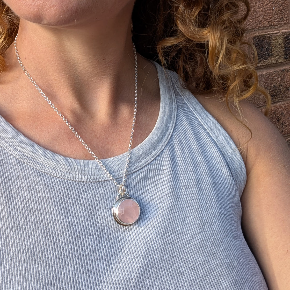 Rose Quartz Statement Gemstone Necklace being worn on a sterling silver chain over a grey top, showing the size and length of the round pink gemstone pendant.