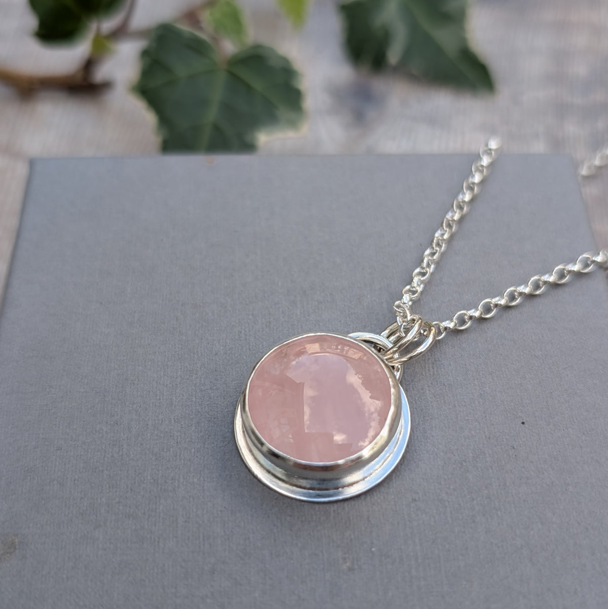Close-up of the Rose Quartz Statement Gemstone Necklace showing the pale pink round gemstone set in a handmade sterling silver bezel on a grey background.