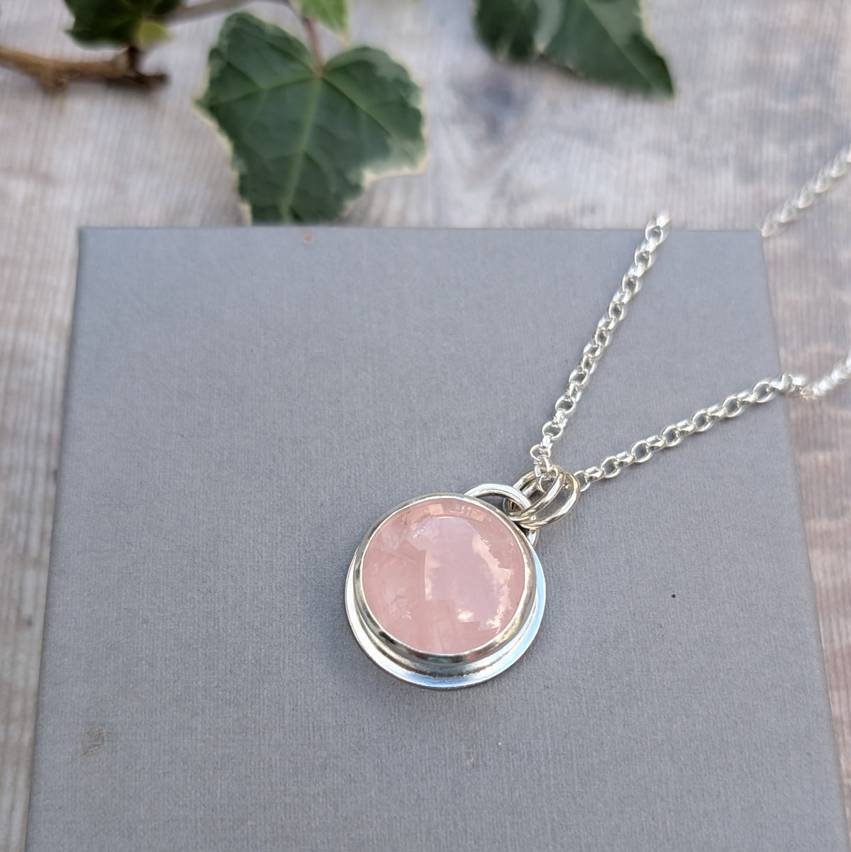 Rose Quartz Statement Gemstone Necklace displayed on a grey background with a sterling silver chain and round pink gemstone pendant.