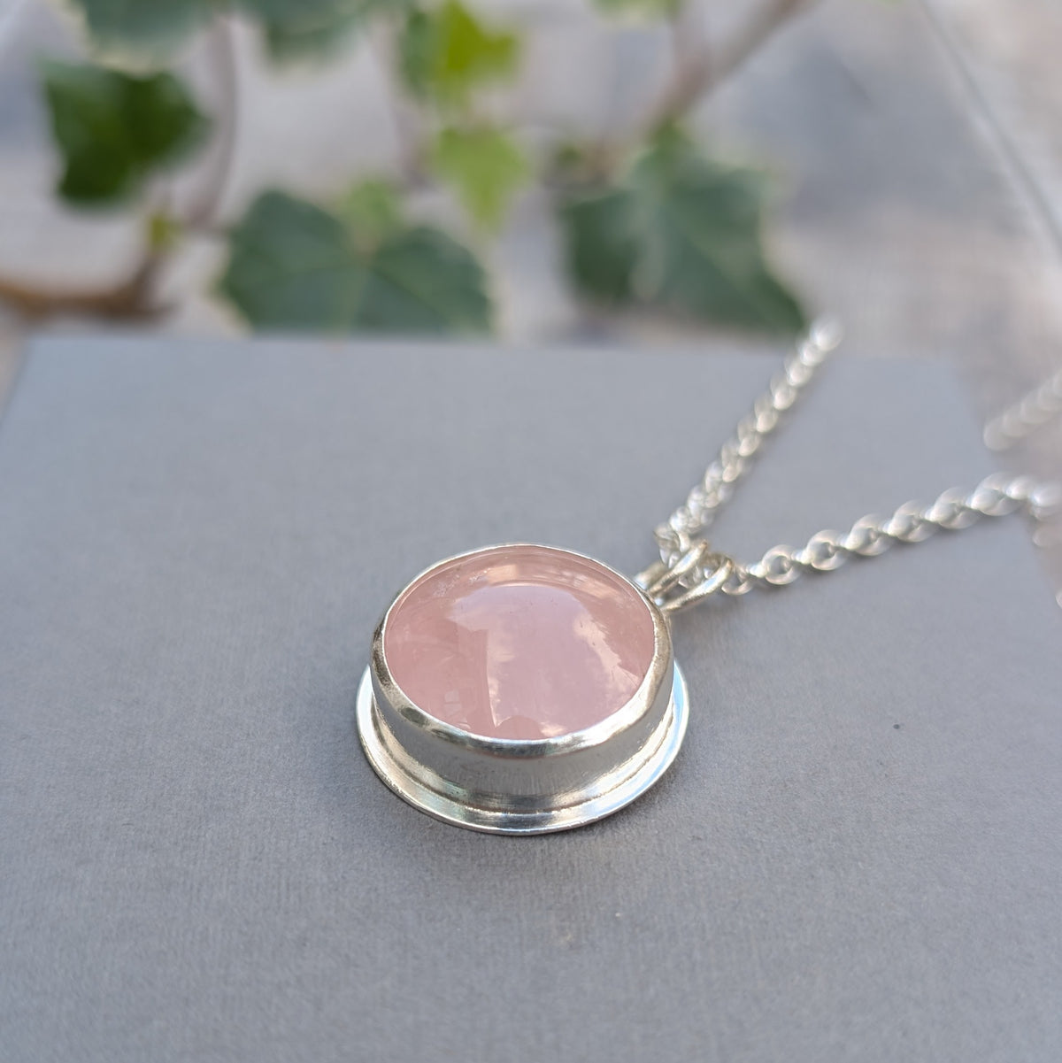 Side view of the Rose Quartz Statement Gemstone Necklace showing the raised silver bezel setting holding the round pale pink gemstone.