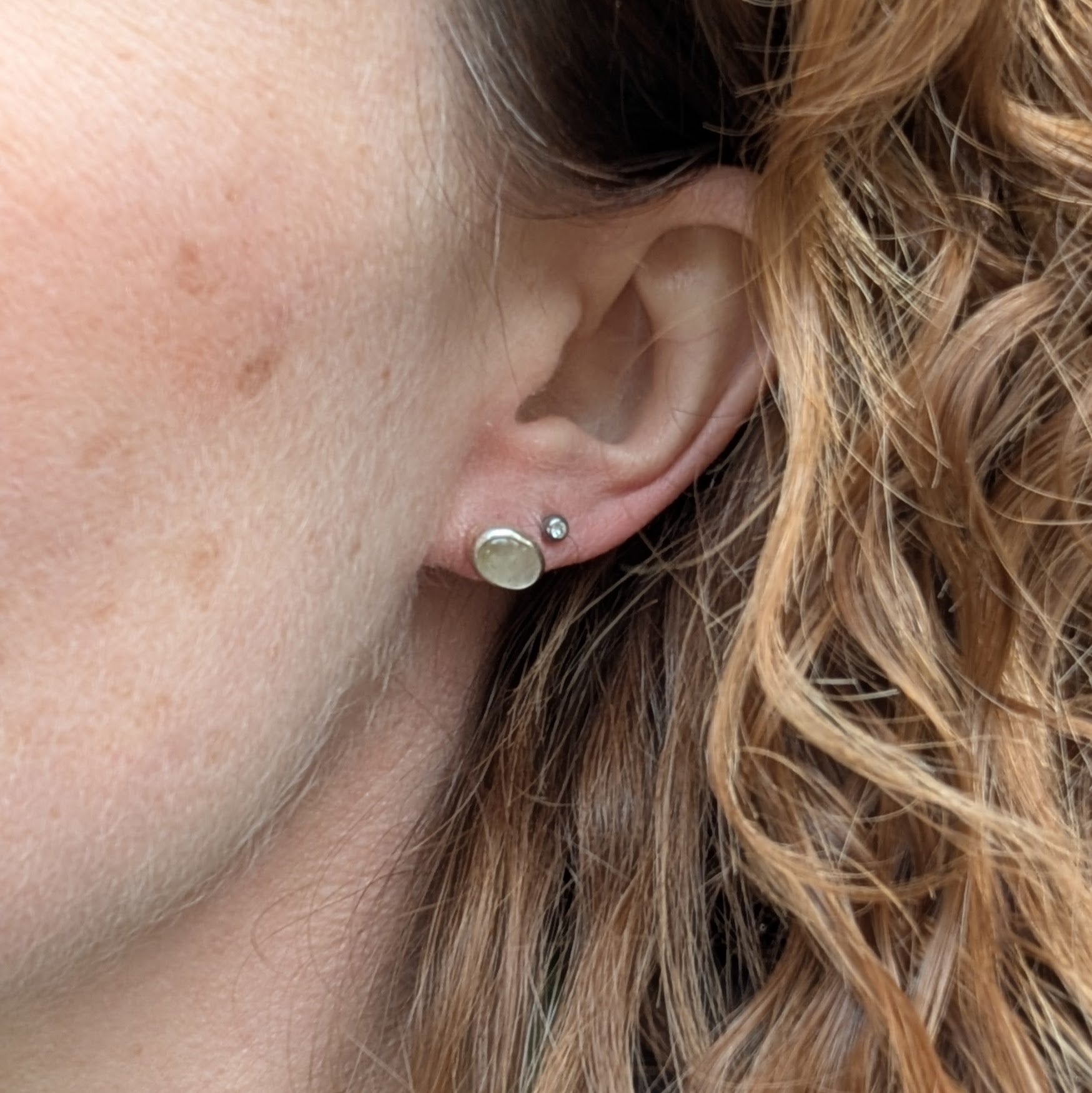 A close-up of a person wearing one of the oval rutile quartz stud earrings, highlighting its size and elegant design alongside a smaller stud.