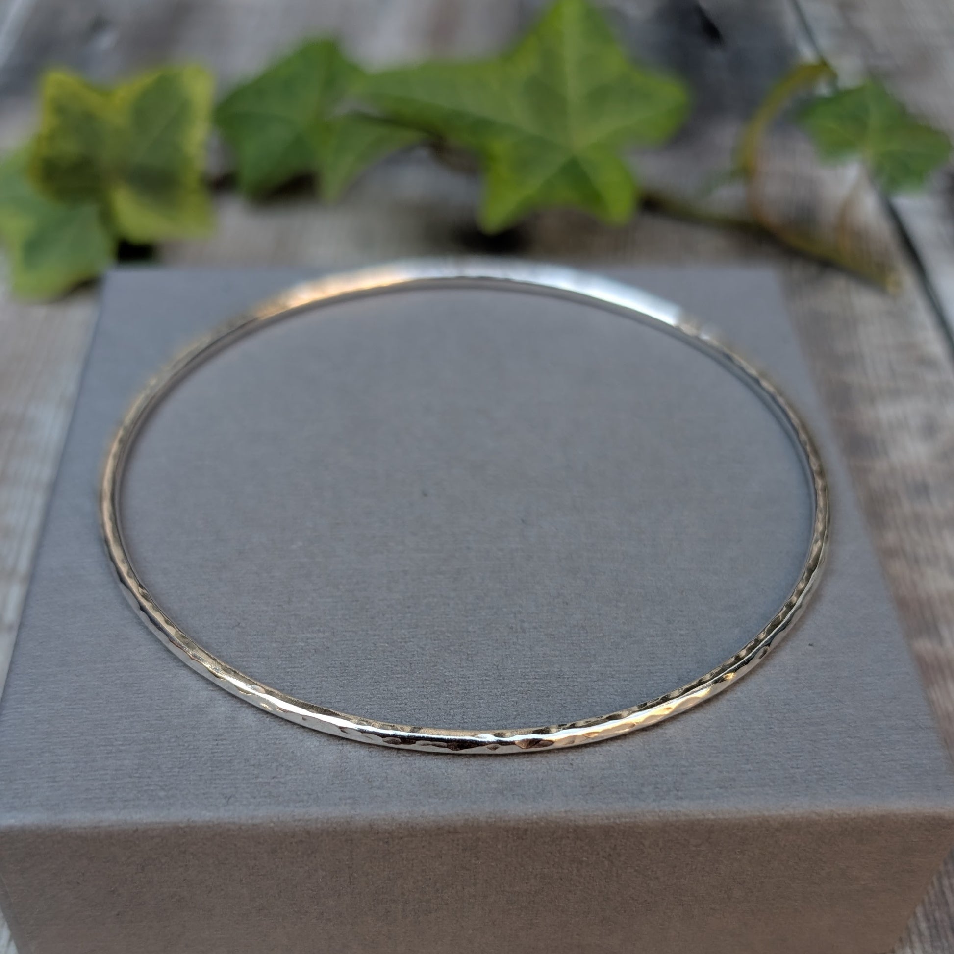 Silver 2mm Hammered Round Bangle shown on a grey jewellery box, with the hand hammered texture visible around the silver bangle.