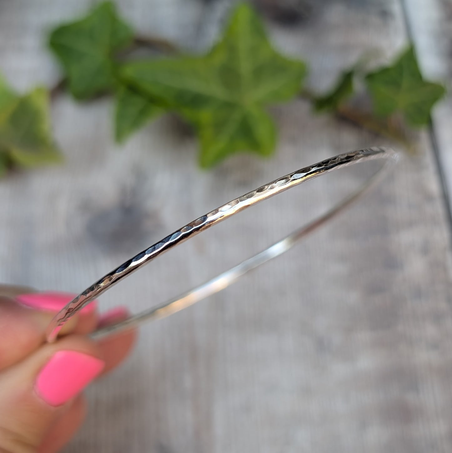 Close up side view of a Silver 2mm Hammered Round Bangle being held, showing the hammered texture along the 2mm silver wire.