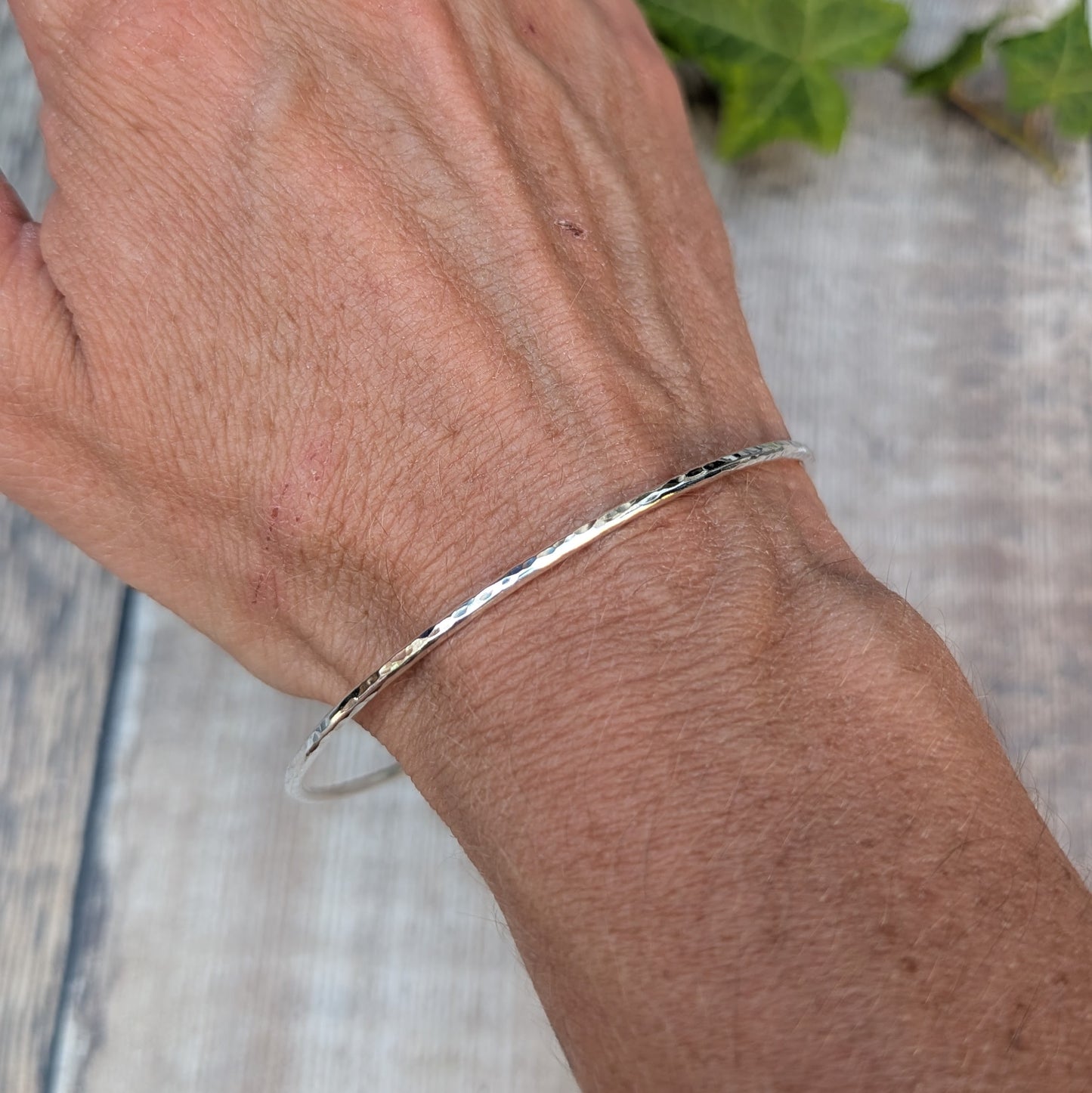 Silver 2mm Hammered Round Bangle worn on the wrist, showing the simple slim design and hand hammered finish.