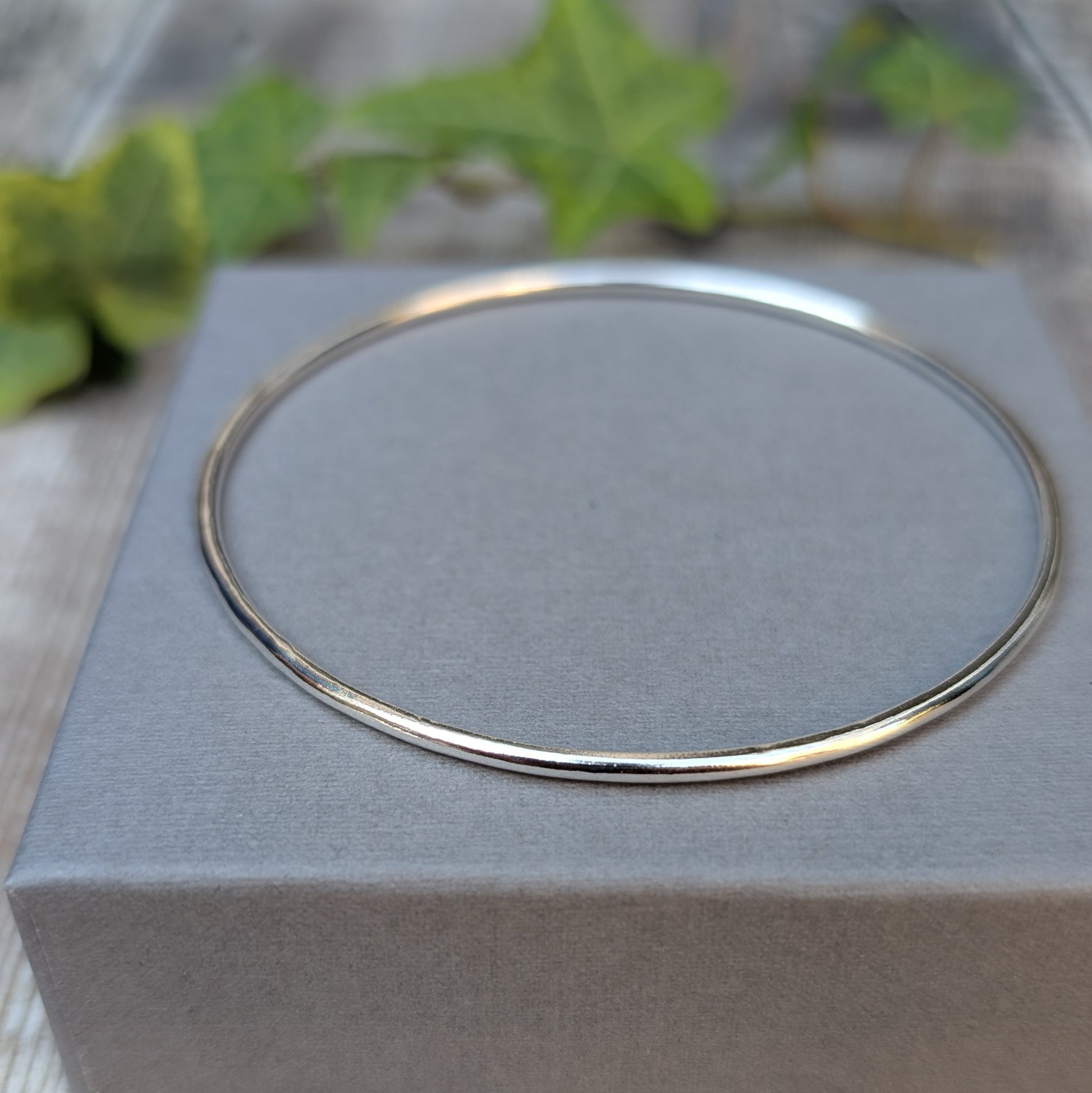 Silver 2mm Smooth Round Bangle displayed on a grey jewellery box, with a close up view of the simple smooth silver design.