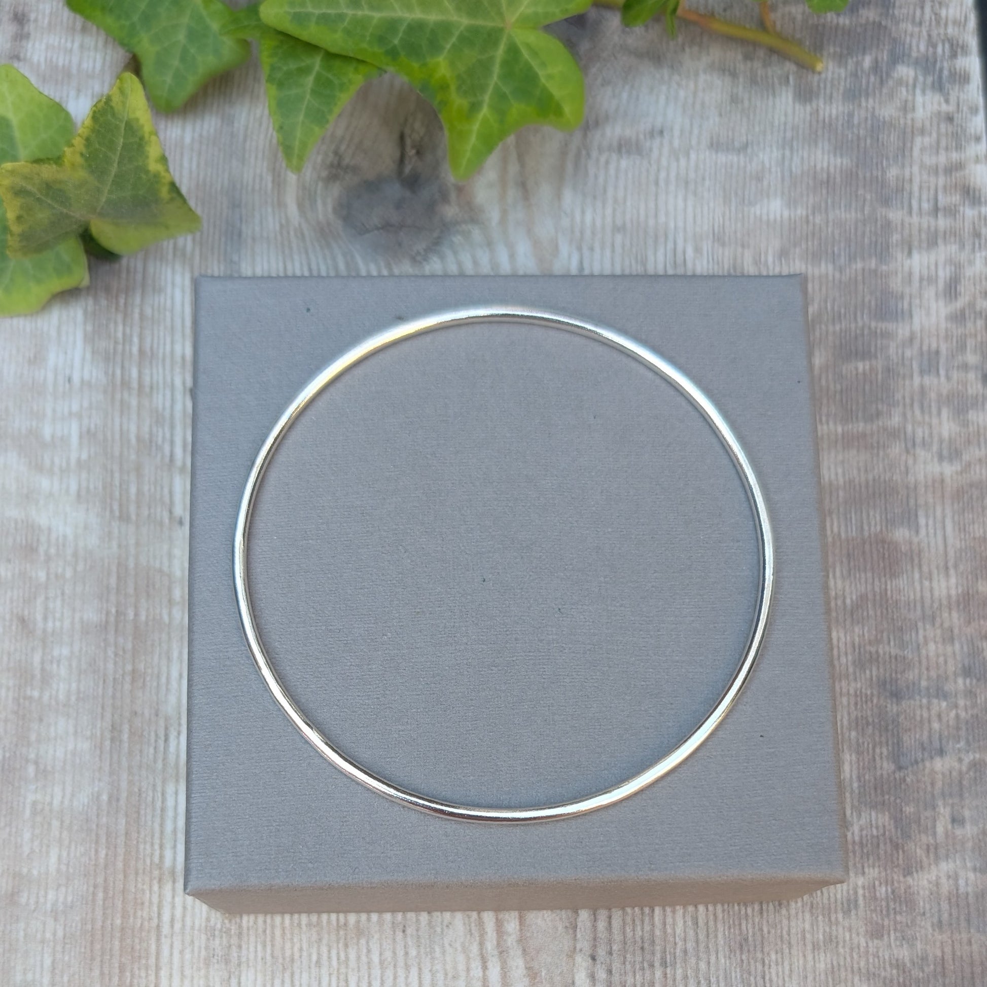 Silver 2mm Smooth Round Bangle shown from above on a grey jewellery box, showing the simple round shape and smooth silver finish.