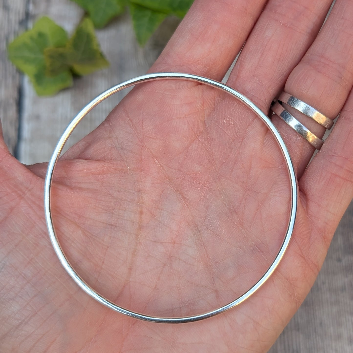 Silver 2mm Smooth Round Bangle held in the palm of a hand, showing the size, round shape and smooth polished finish.