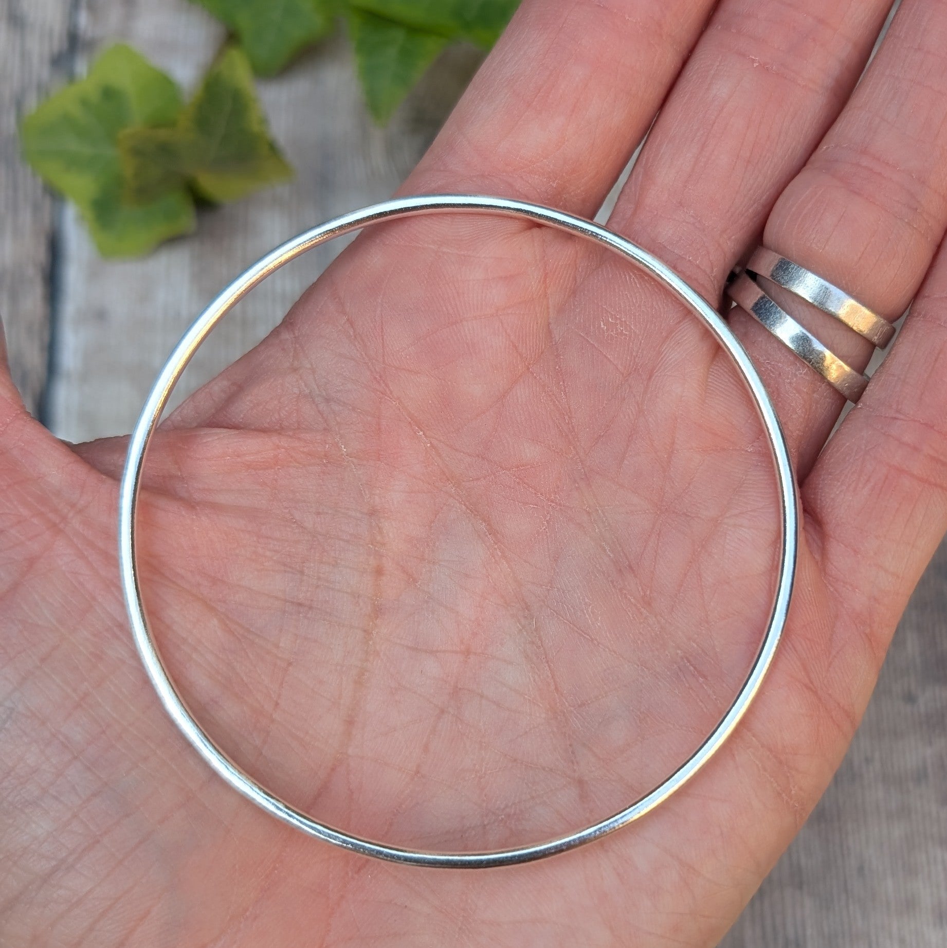 Silver 2mm Smooth Round Bangle held in the palm of a hand, showing the size, round shape and smooth polished finish.