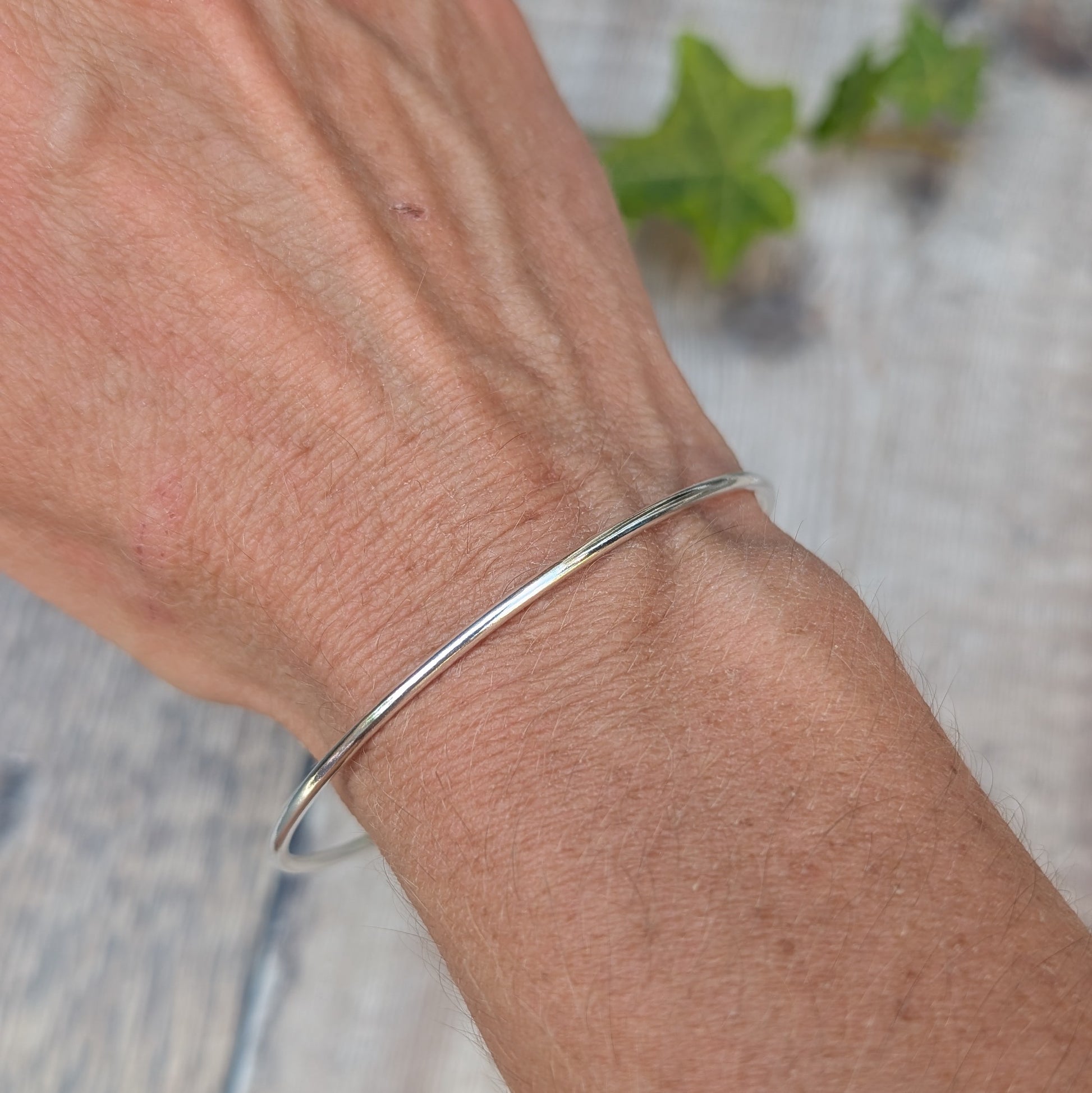 Silver 2mm Smooth Round Bangle handmade from recycled Sterling Silver, shown being worn on the wrist to show the simple smooth design and fit.